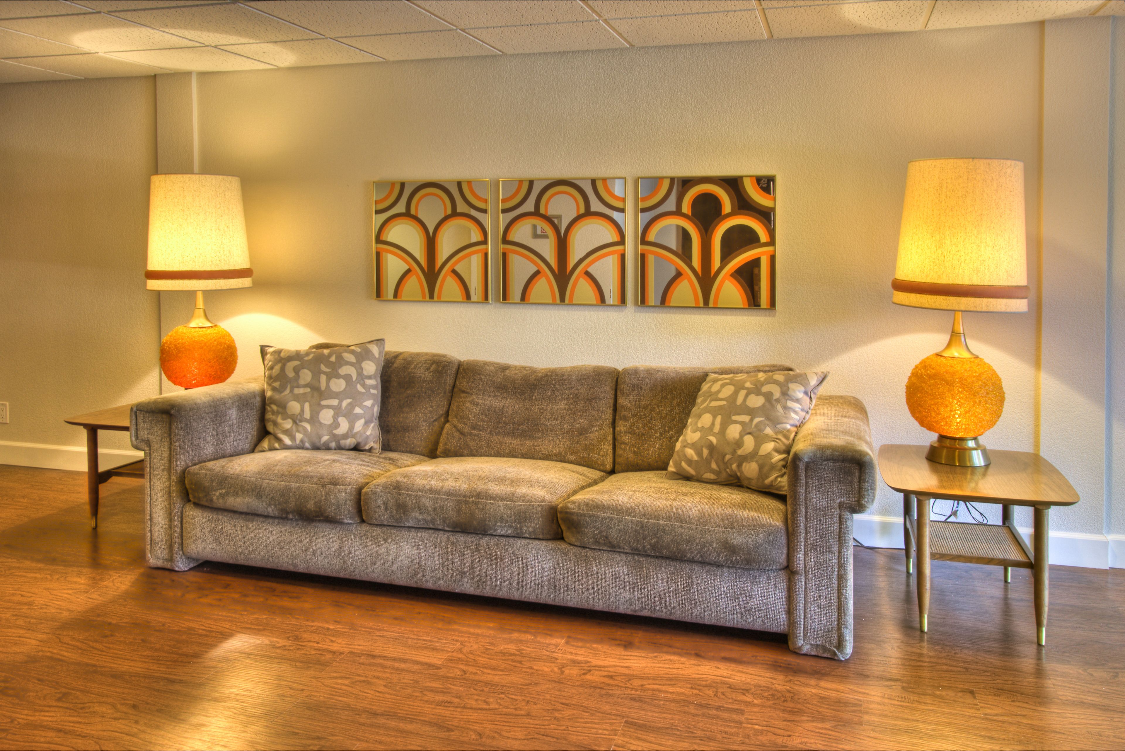 A modern living room with a grey sofa, patterned cushions, and two lamps with orange bases.