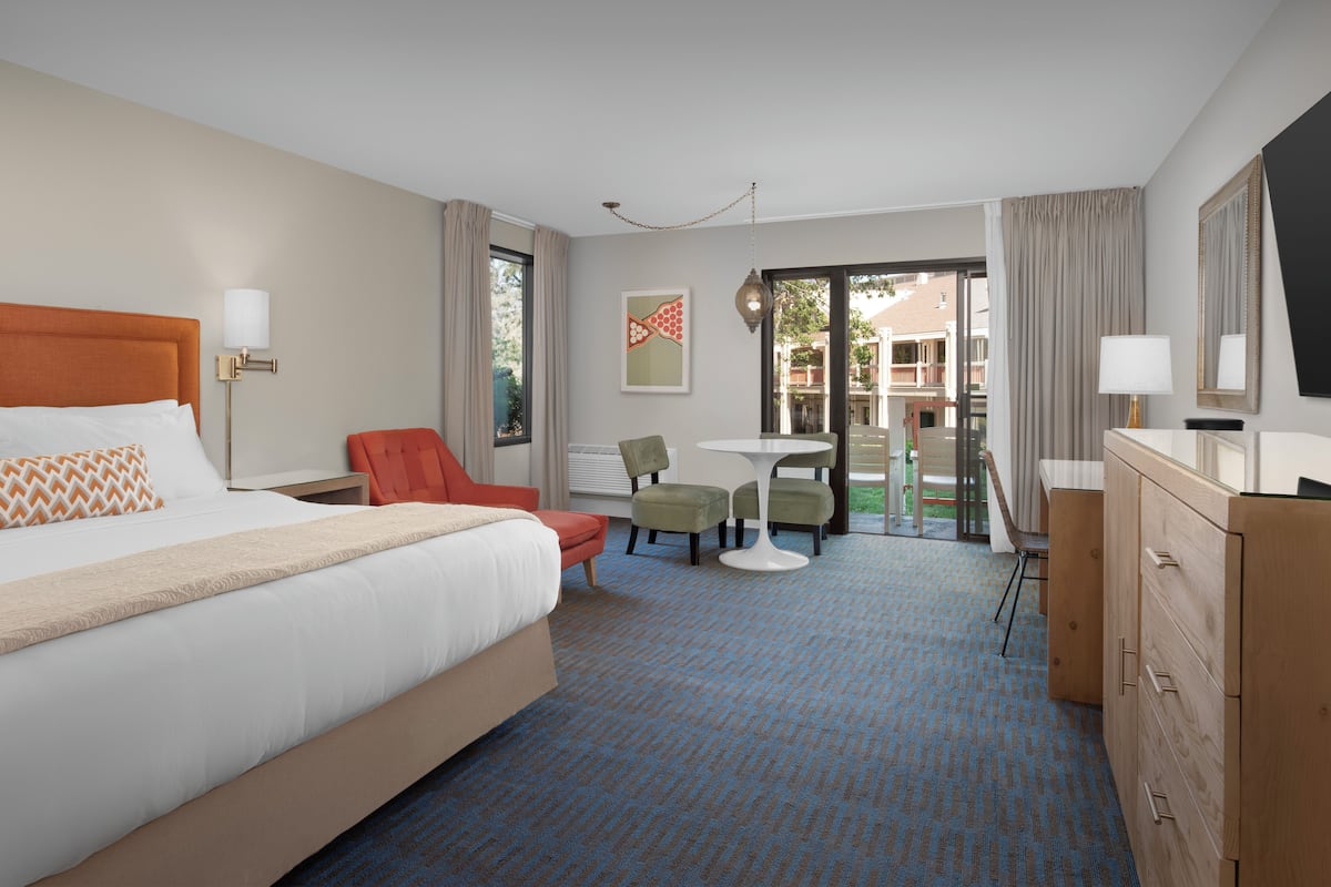A hotel room with a large bed, a desk, two chairs, a dresser, and a television.