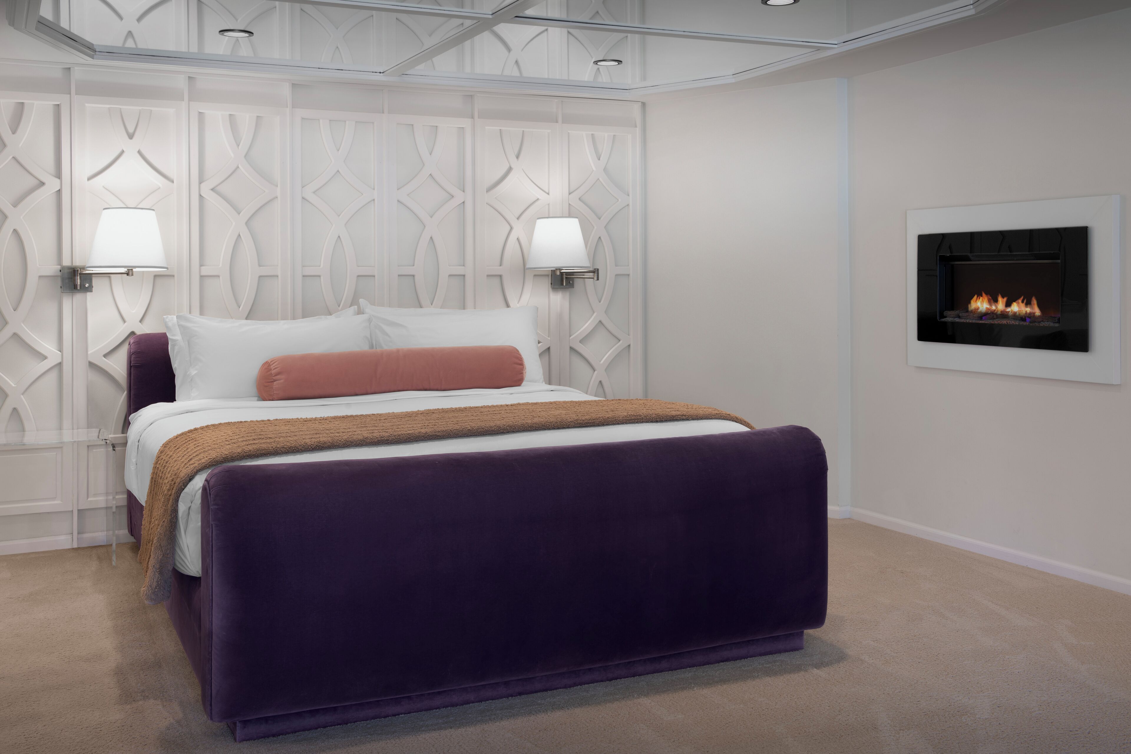 A modern bedroom with a large bed, two wall-mounted lamps, and a fireplace.