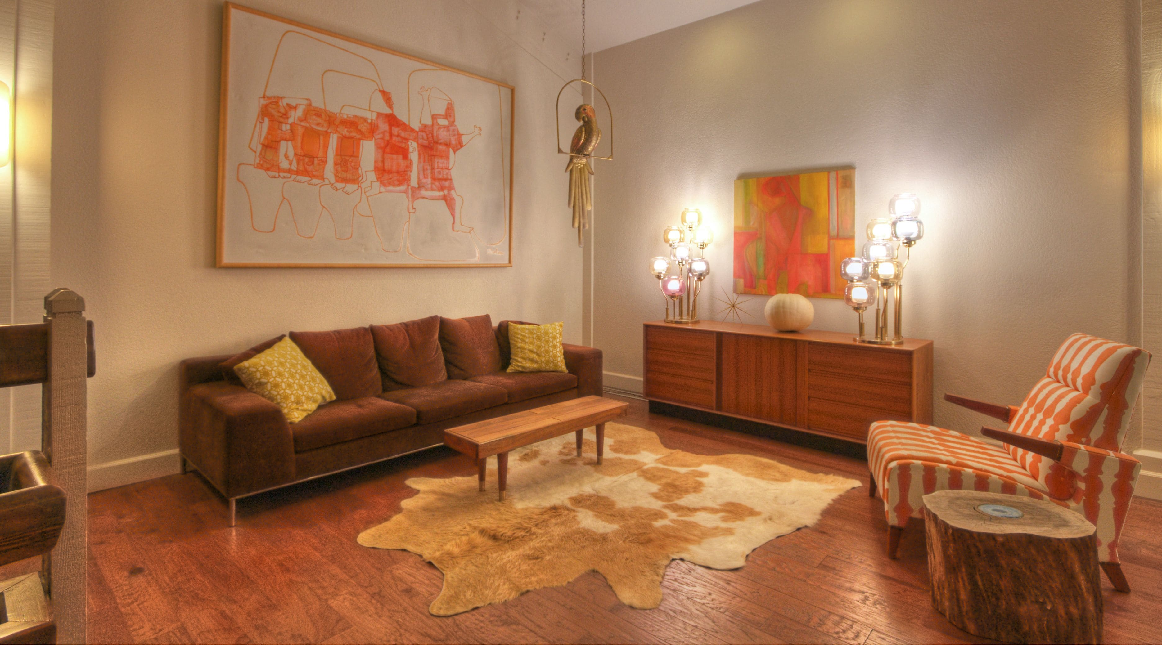 A living room with a brown sofa, a wooden bench, a cowhide rug, a wooden cabinet, and a chair with a striped pattern.