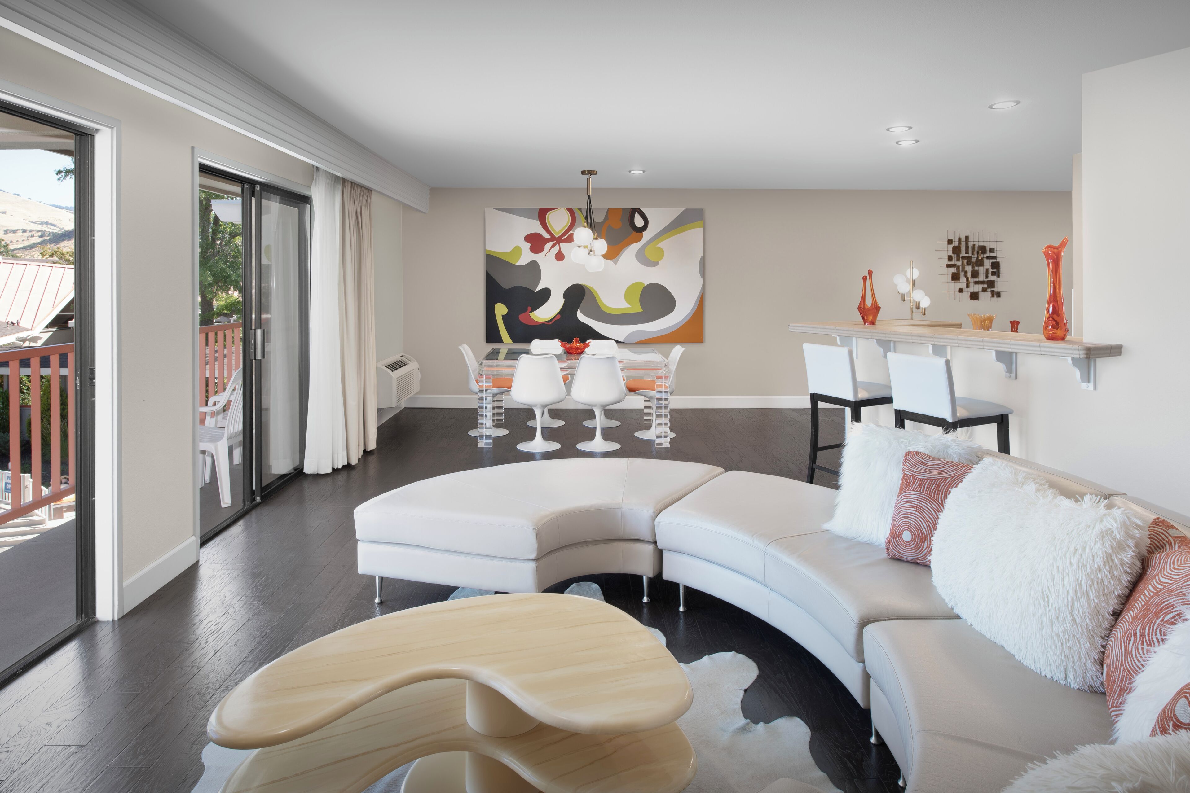 Un salon moderne avec un canapé blanc aux lignes courbes, une table basse en bois et un coin repas comprenant une table et des chaises blanches.