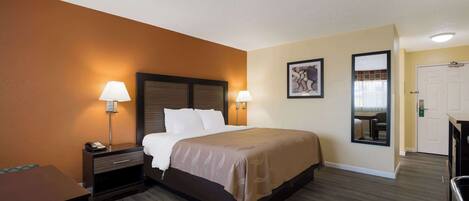 A hotel room with a bed, two bedside lamps, a nightstand, a desk, and a chair.