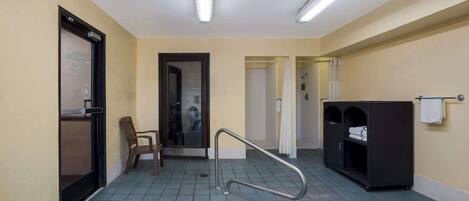 A hotel bathroom with a tiled floor, a shower area, a sink, a towel rack, and a storage cabinet.