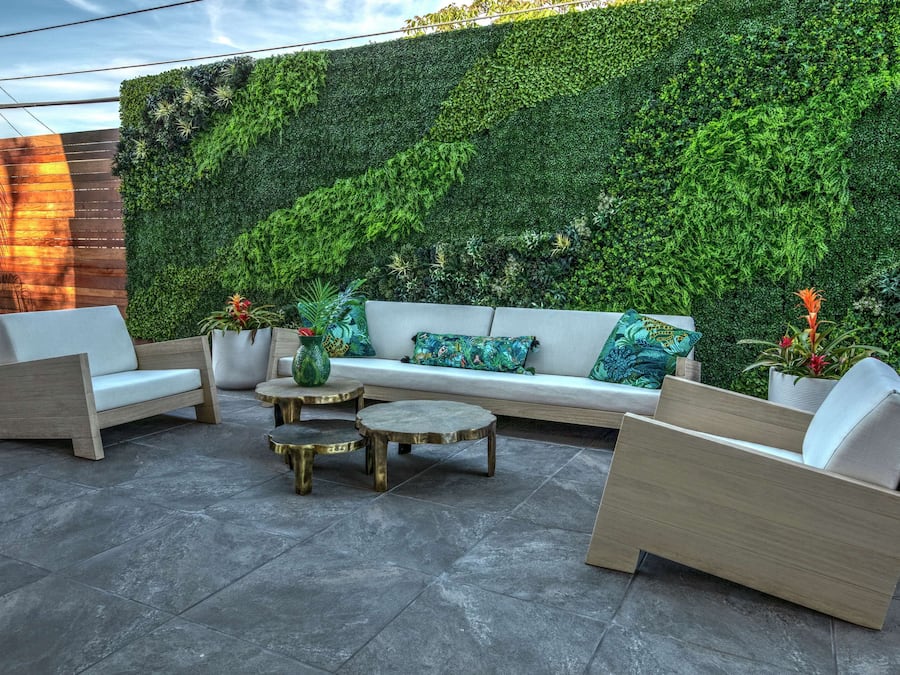 Uma área de estar moderna ao ar livre, com um jardim vertical verde, assentos acolchoados e mesas redondas.