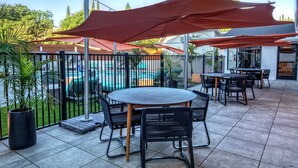 An outdoor patio with a pool, tables, chairs, and umbrellas.