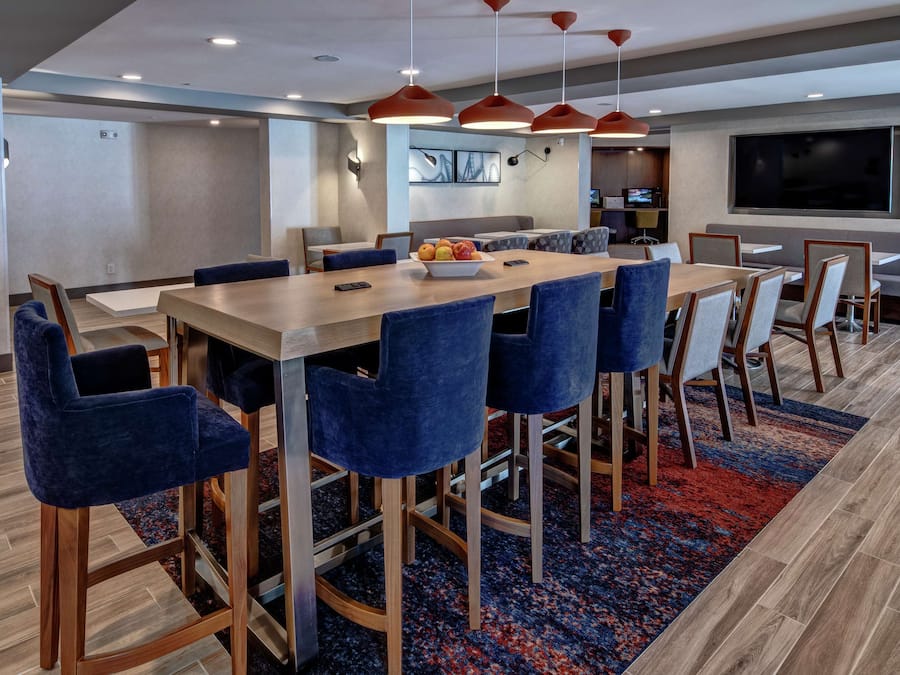 A modern dining area with a long table, blue upholstered chairs, and a red carpet.
