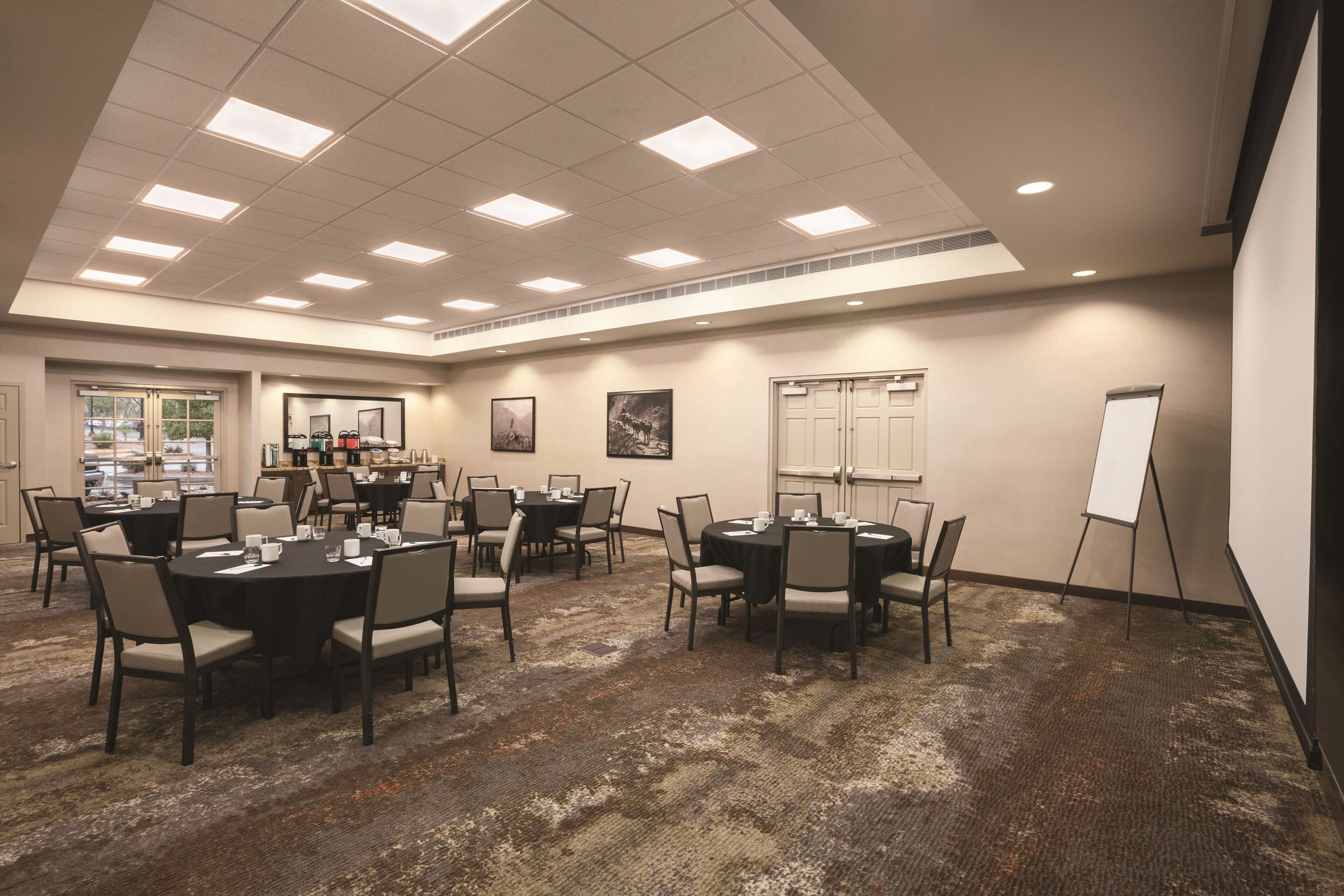 A conference room with round tables, chairs, a whiteboard, and a carpeted floor.