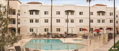 A hotel with a pool area, palm trees, and outdoor seating.