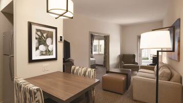 Quarto de hotel com mesa de jantar, cadeiras, sofá, televisão e abajur.