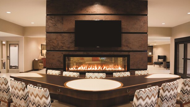 A modern living room with a large fireplace, a flat-screen TV mounted on the wall, and a round dining table surrounded by chairs. - Homewood Suites by Hilton Tucson/St. Philip's Plaza Univ (Tucson)