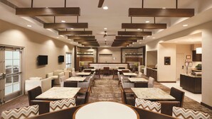 A spacious hotel lobby with multiple seating areas, a central dining table, and a kitchen area visible in the background. - Homewood Suites by Hilton Tucson/St. Philip's Plaza Univ (Tucson)