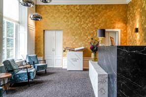 A reception area with a marble counter, two blue armchairs, a white cabinet, and a patterned wall.