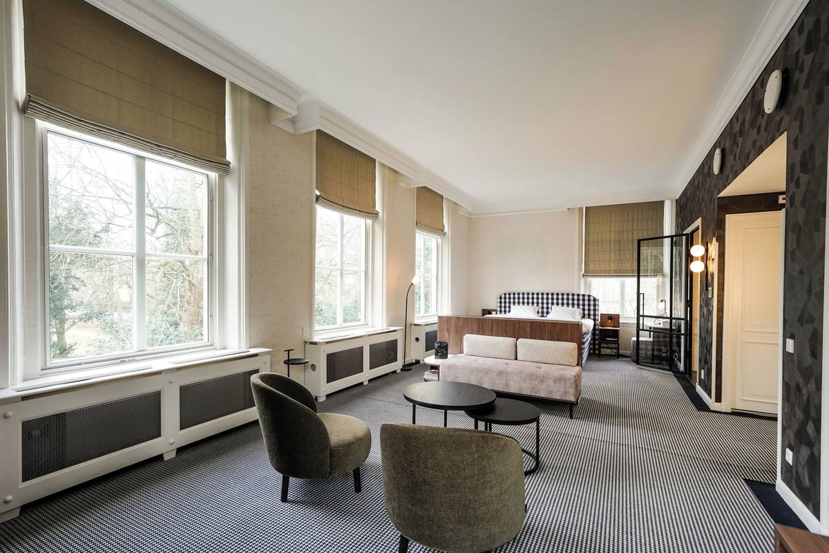 Een moderne hotelkamer met grote ramen, een bank, een salontafel en een eethoek.