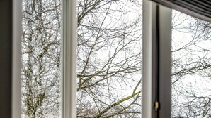 Udsigt gennem et glasdør til et sneklædt udendørsareal med gelænder og en urne med lilla blomster.