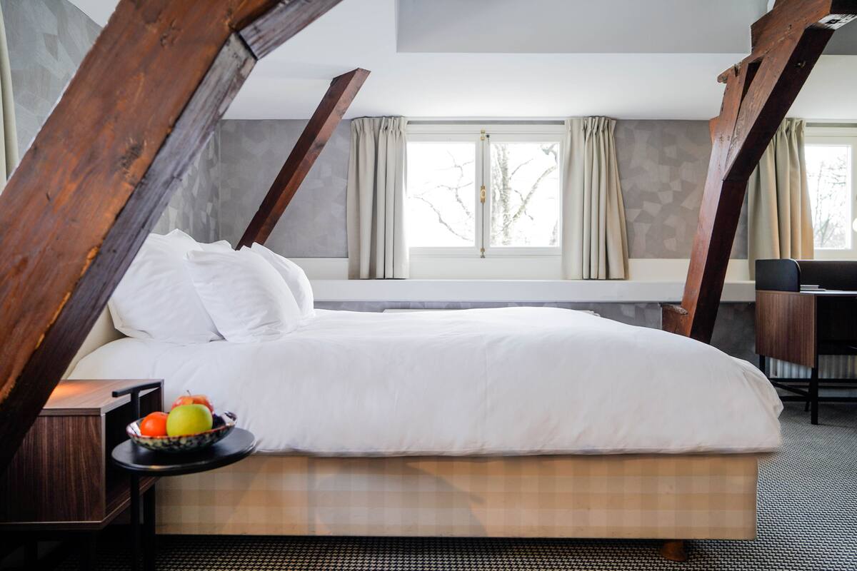 Een slaapkamer met een groot bed, een nachtkastje met een fruitschaal en een bureau met een stoel.