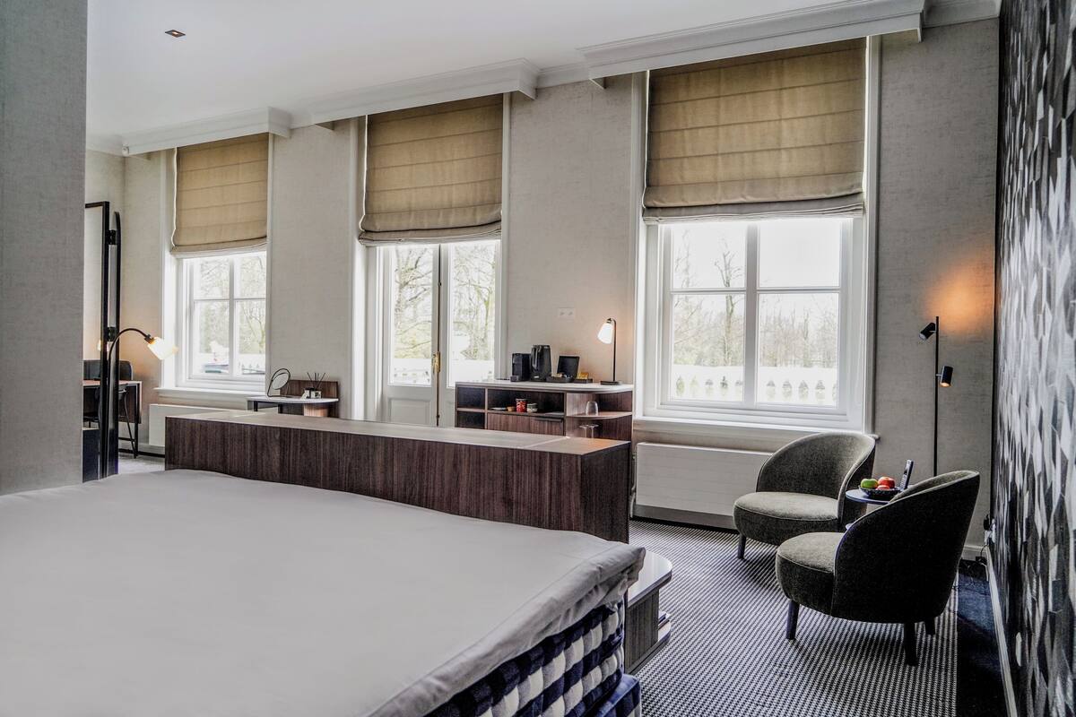 Een hotelkamer met een groot bed, een bureau en een zithoek bij het raam.