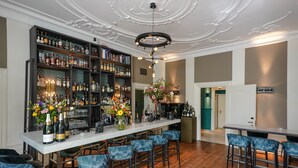 En bar med en marmorplade, flere hylder med flasker og blå barstole.