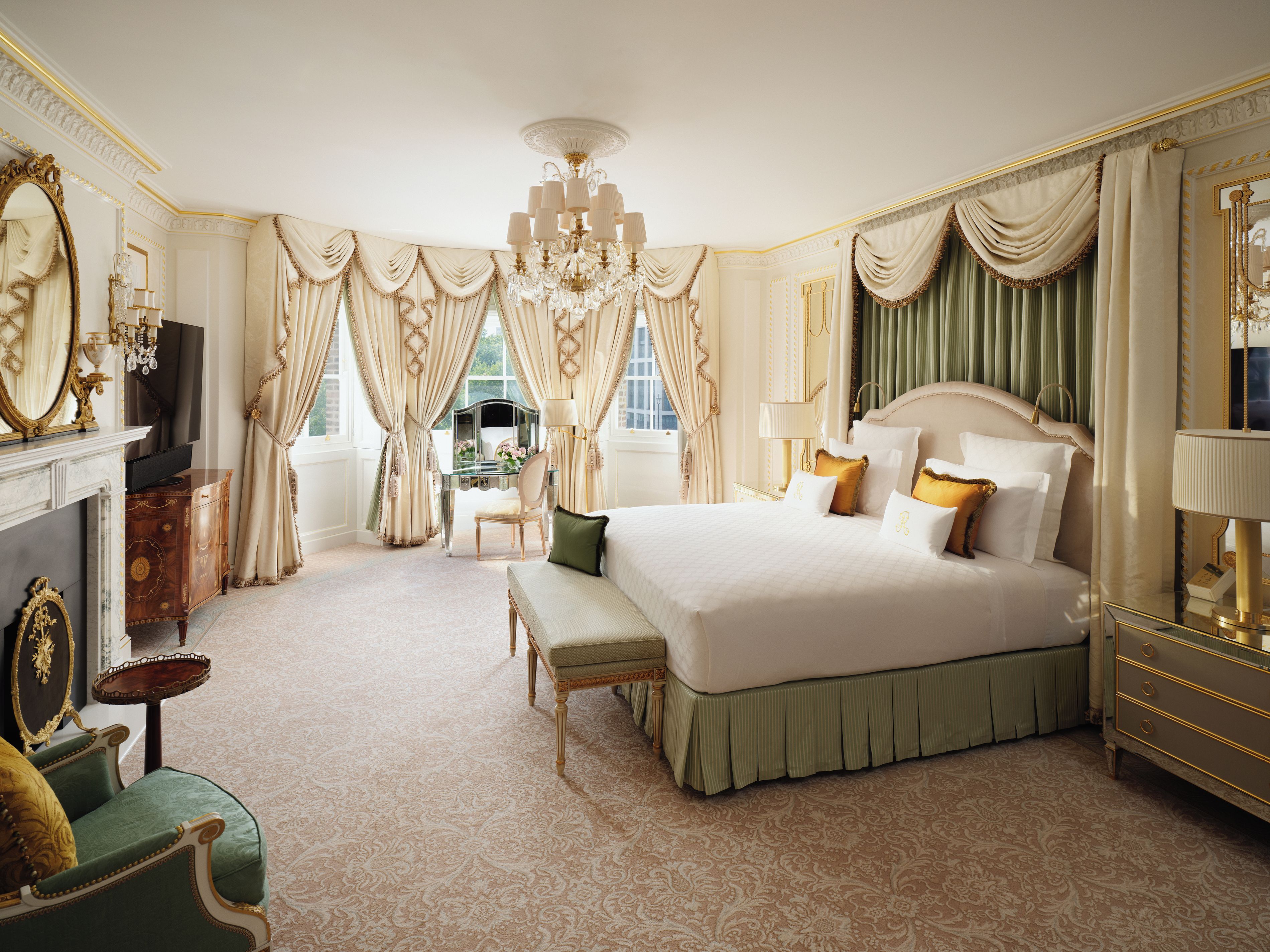 A luxurious bedroom with a large bed, a vanity with a mirror, a desk, and a chandelier.