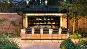 Un bar en plein air avec un mur en briques, une clôture en métal et un jardin planté.