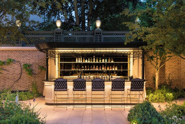 Un bar al aire libre con pared de ladrillo, cerca metálica y jardín con plantas.