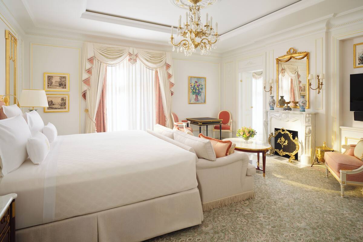 A spacious bedroom with a large bed, a sitting area with a table, and a fireplace.