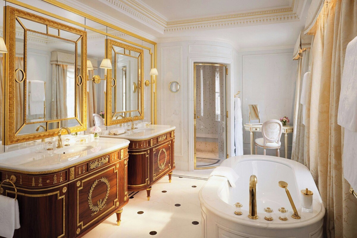A luxurious bathroom with two ornate wooden cabinets, a large freestanding bathtub, and a mirror with a gold frame.