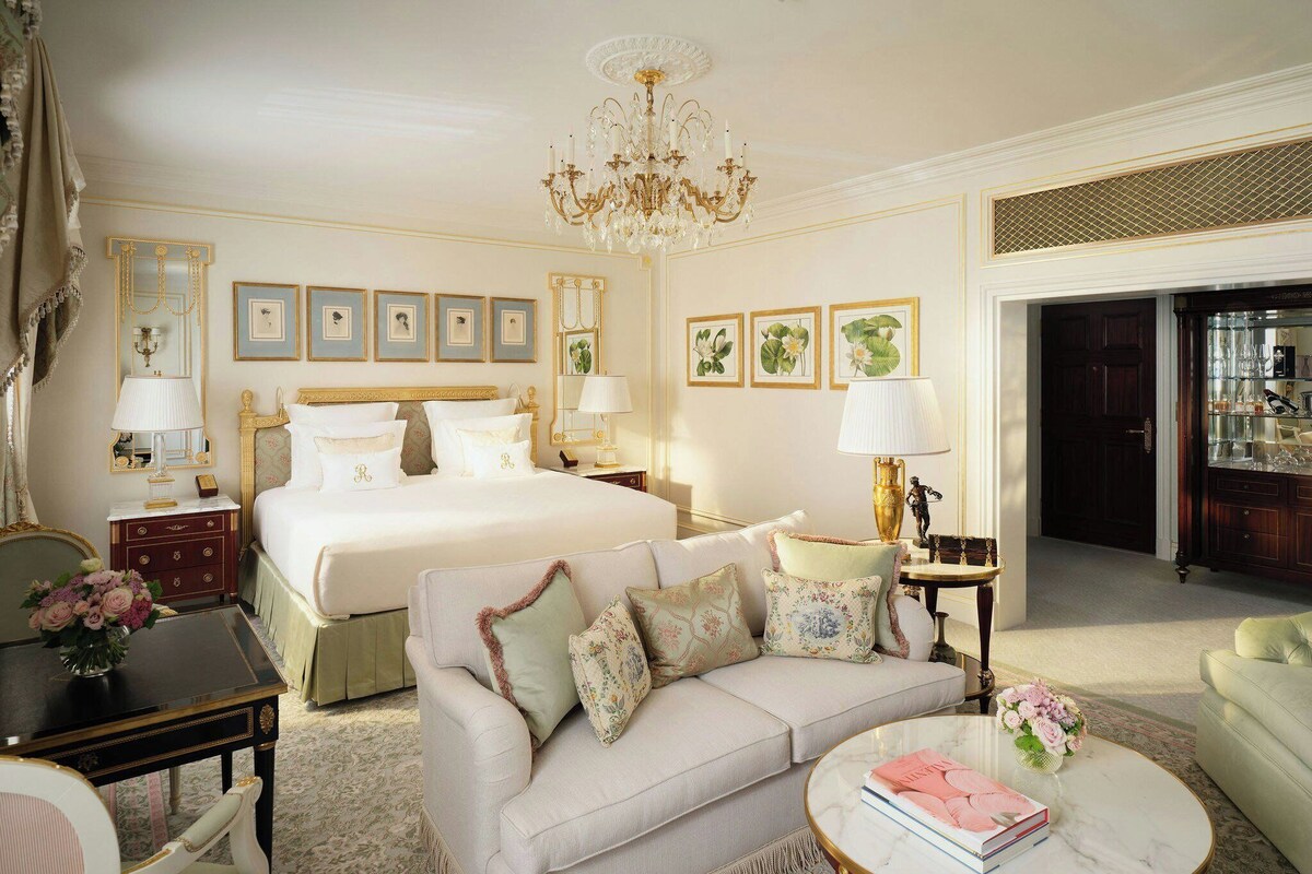 A hotel room with a large bed, a sofa, a coffee table, and a chandelier.