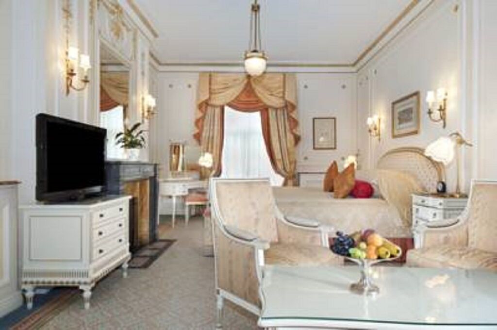 A hotel room with a bed, a TV, a dining table with fruit, a chair, a dresser, and a mirror.