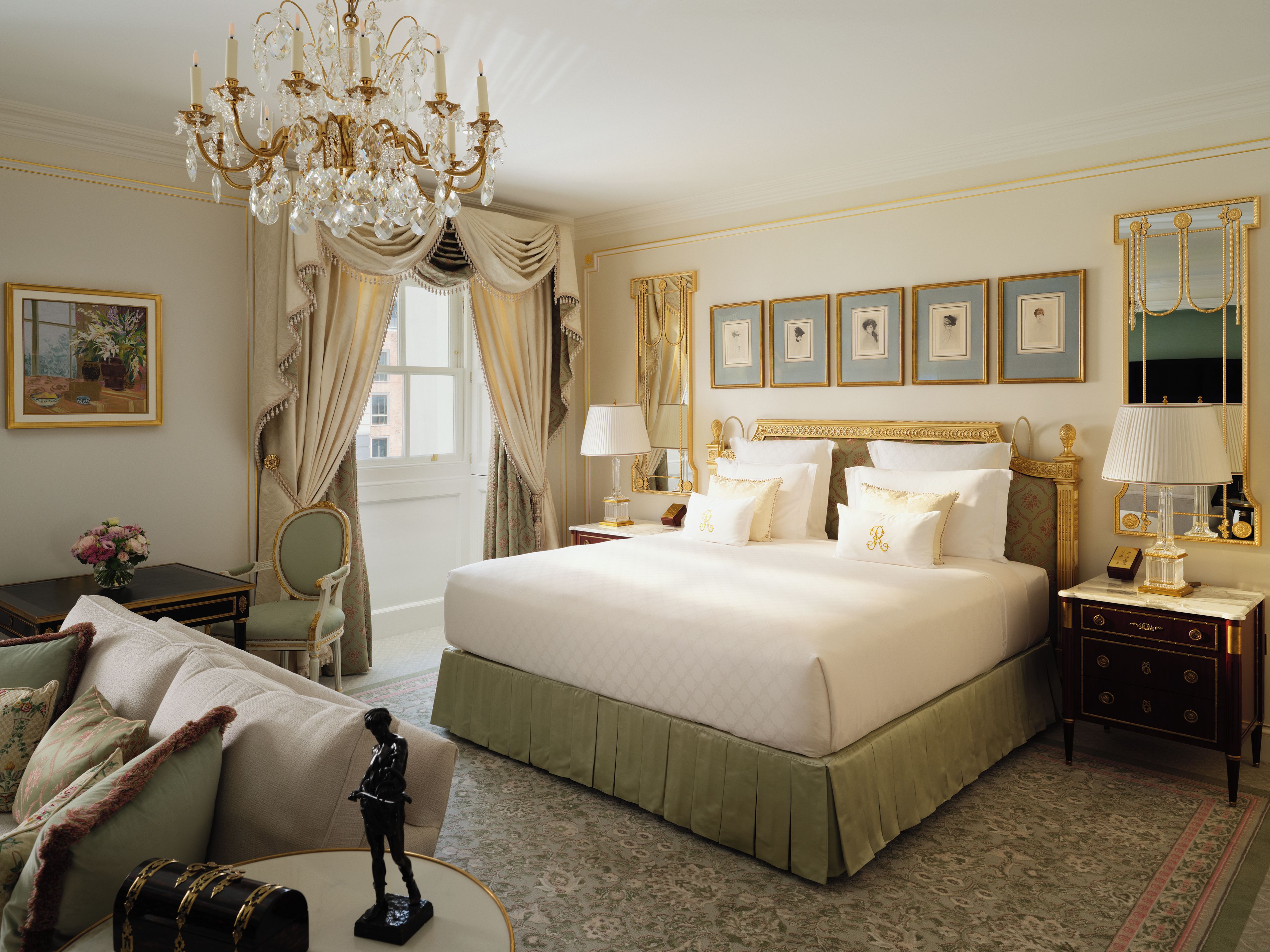 A spacious bedroom with a large bed, a chandelier, and a view of the city.