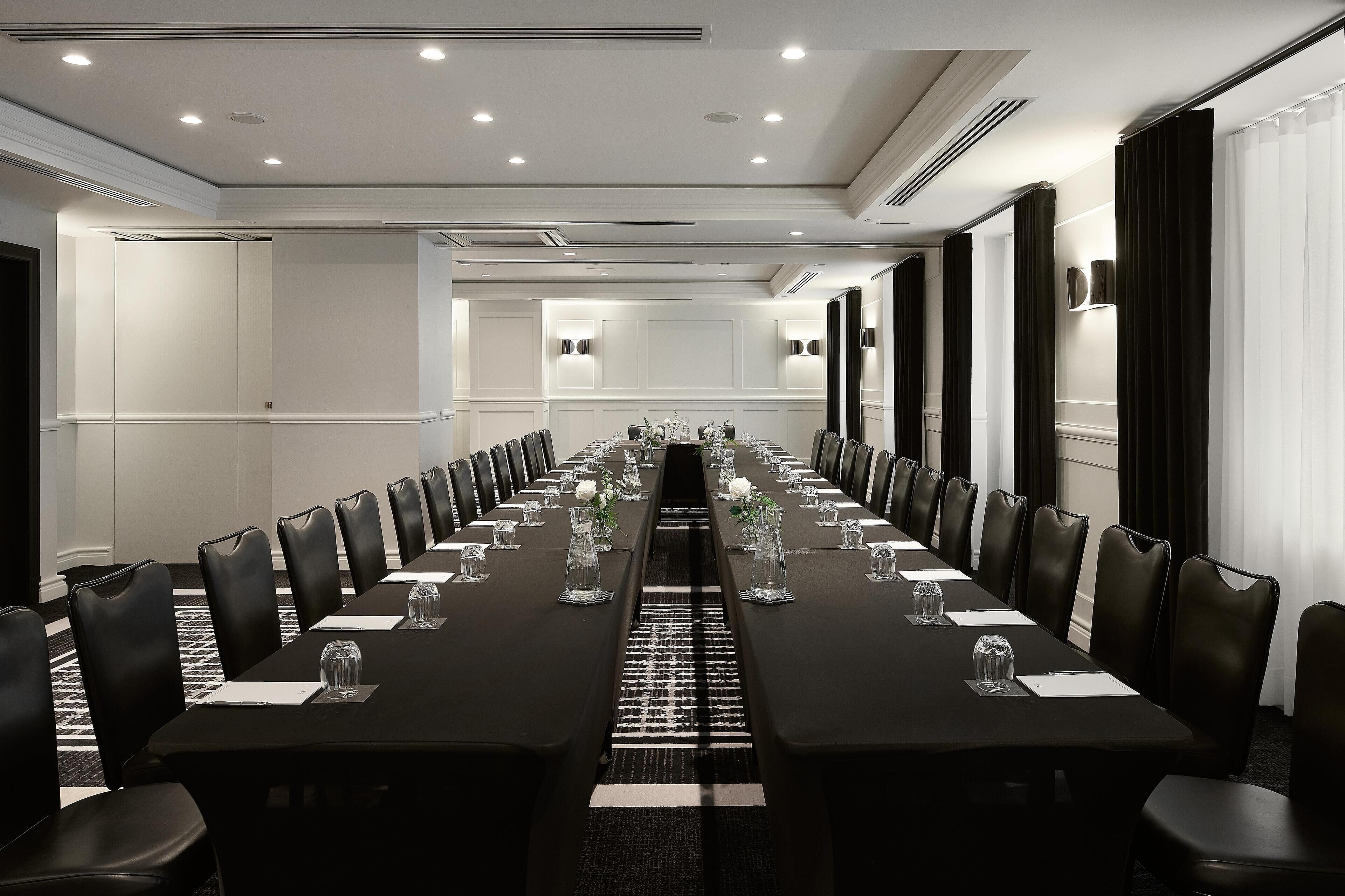 A conference room with a long table, black chairs, and white walls.