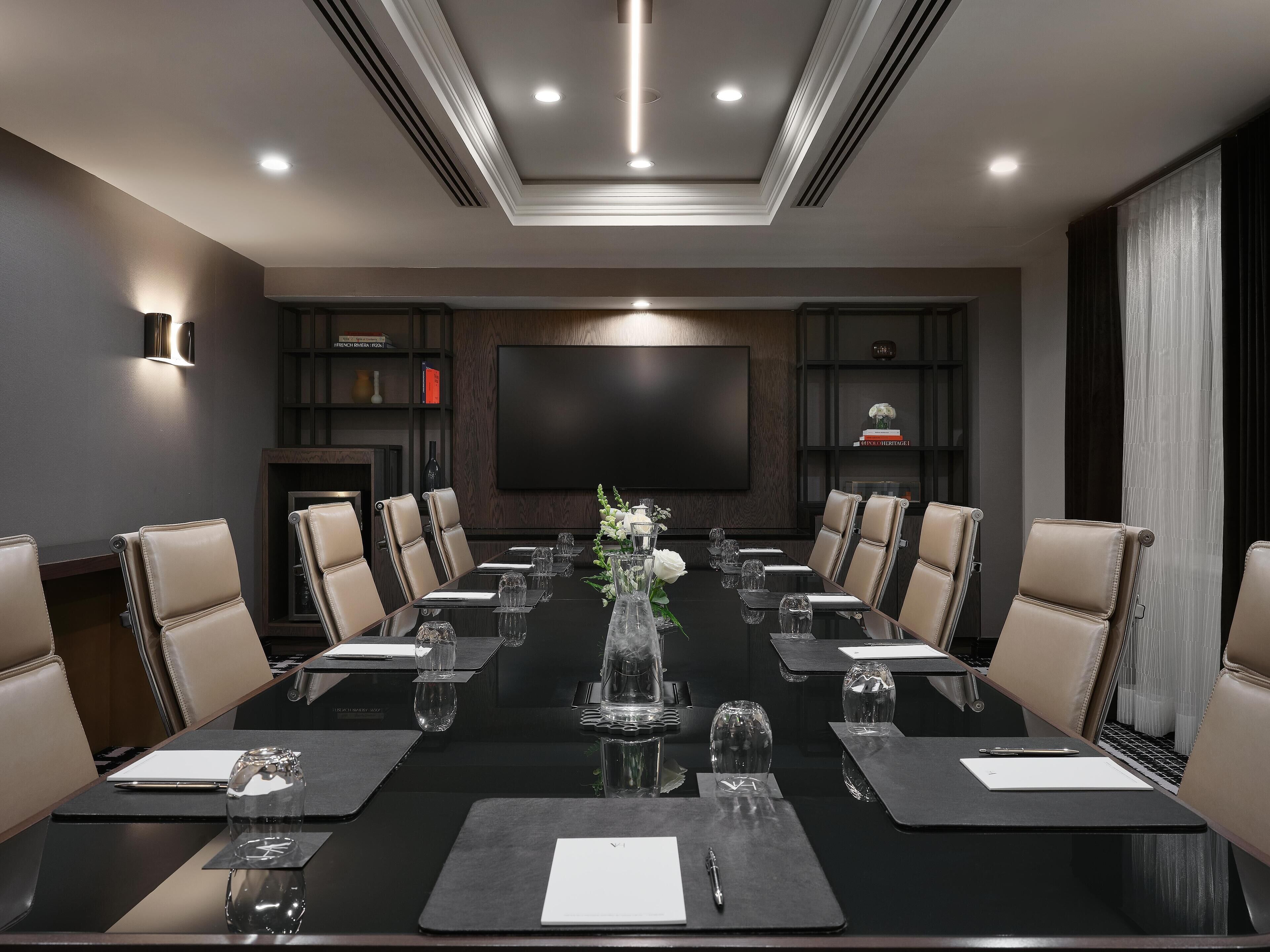 A conference room with a long table, leather chairs, a large flat-screen TV, and a fireplace.