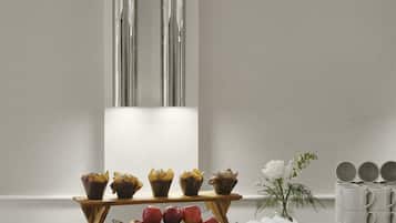 A wooden table with a bowl of fruit, a vase with flowers, and a stack of white mugs.