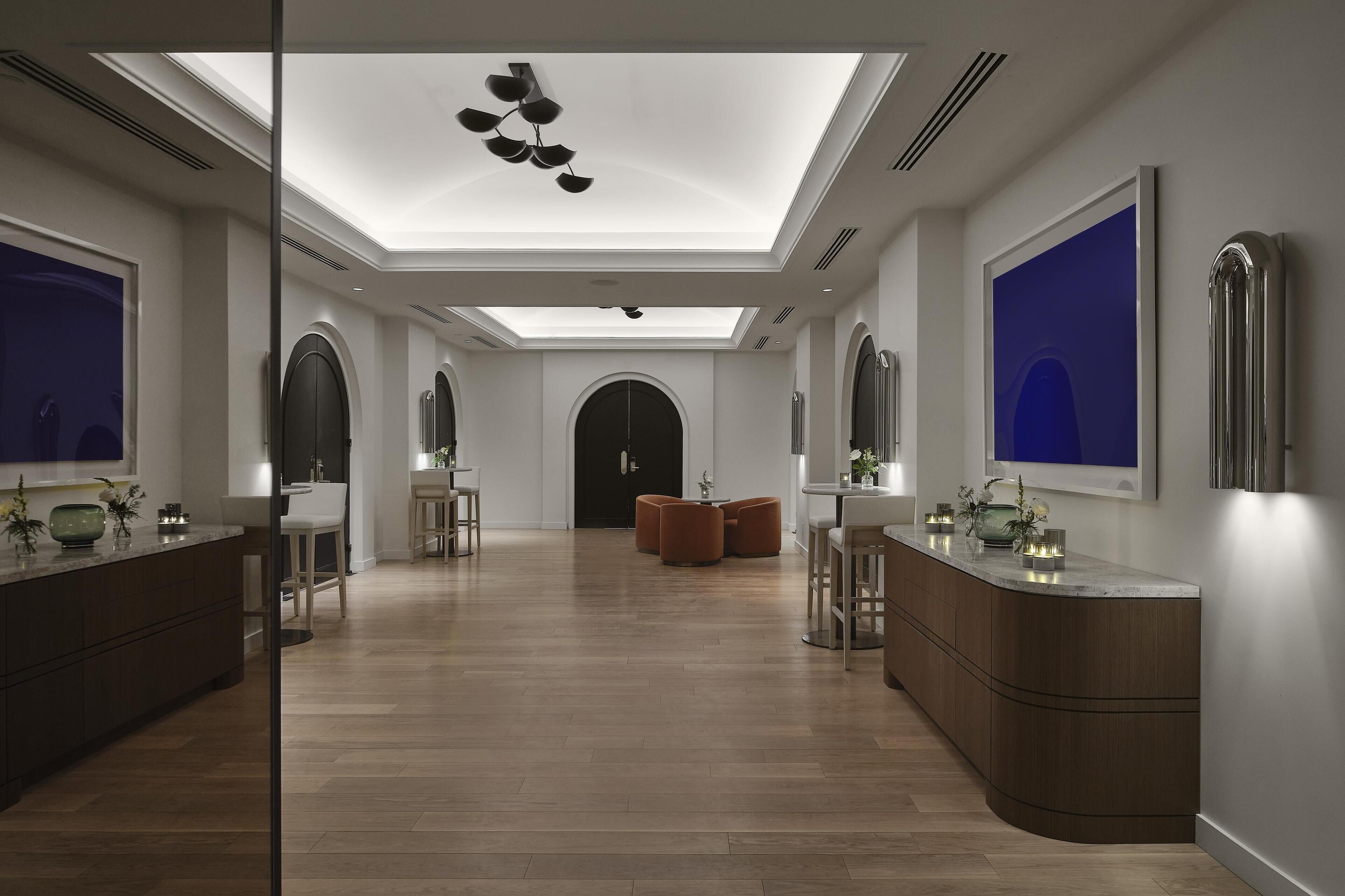 A modern hotel lobby with a skylight, wooden flooring, a central seating area, and a large mirror.