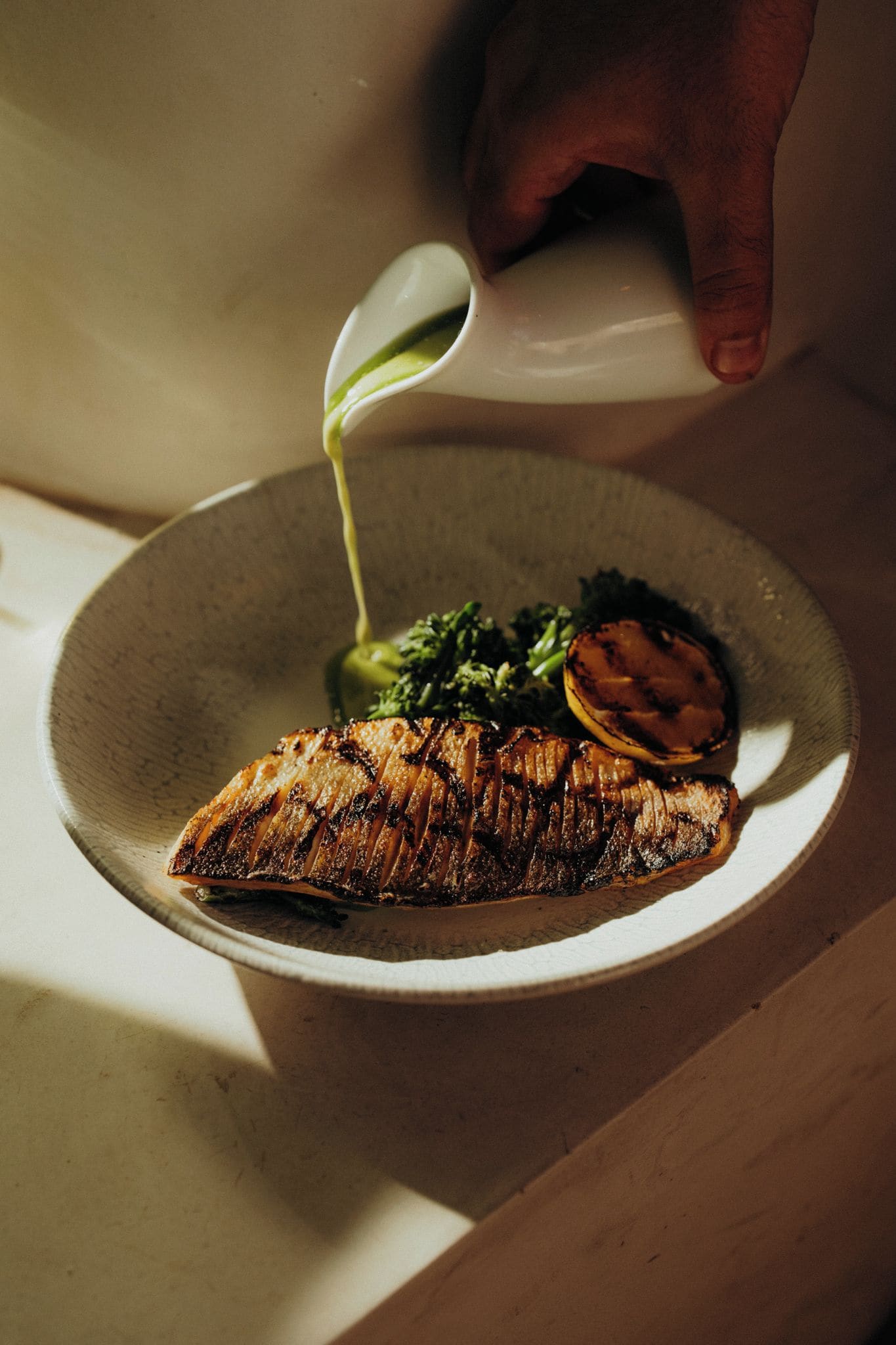 A plate with grilled fish, vegetables, and a slice of lemon on a ceramic dish.