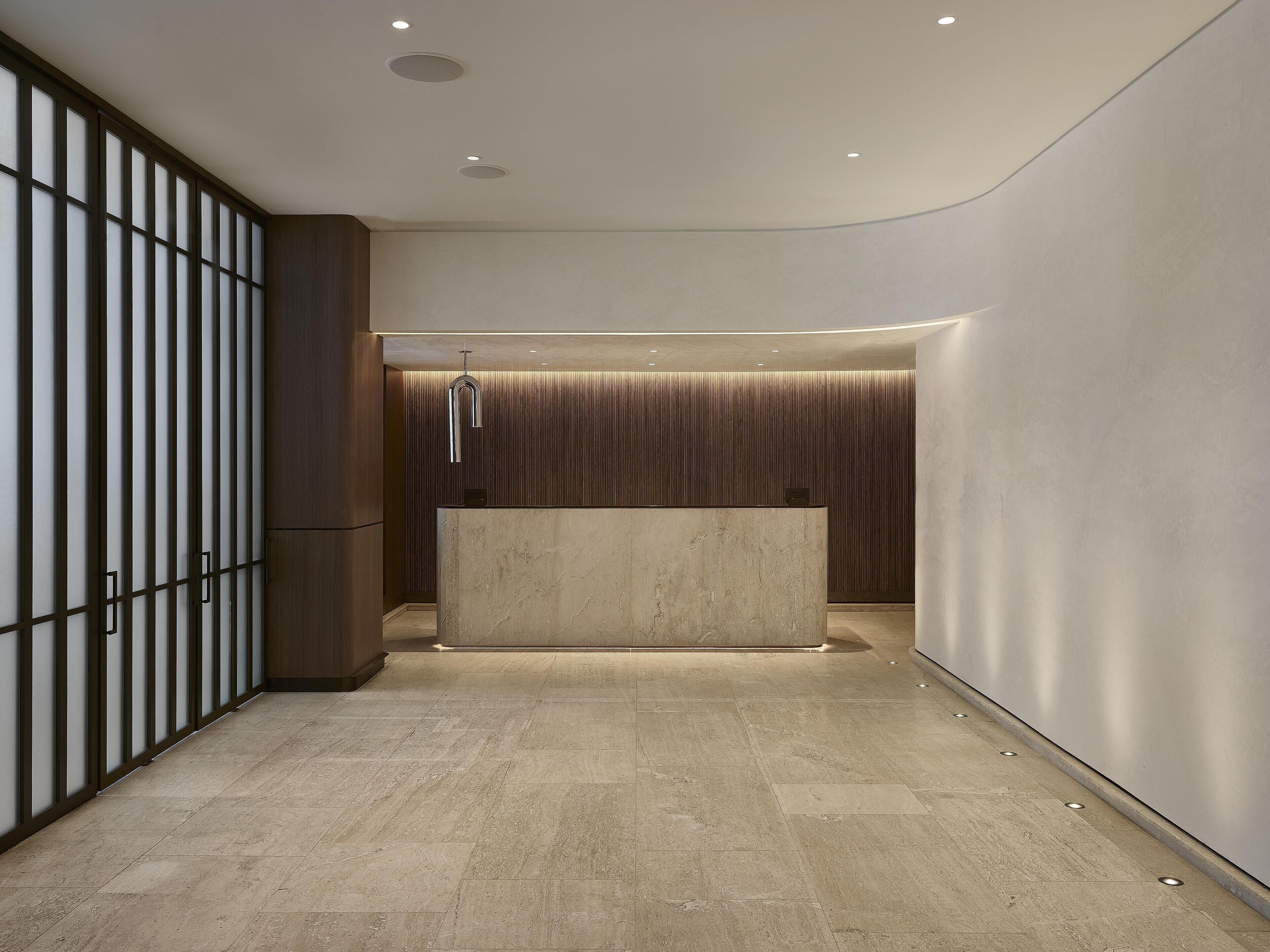 Una moderna zona de recepción con mostrador de mármol, iluminación empotrada y un panel de pared de madera.