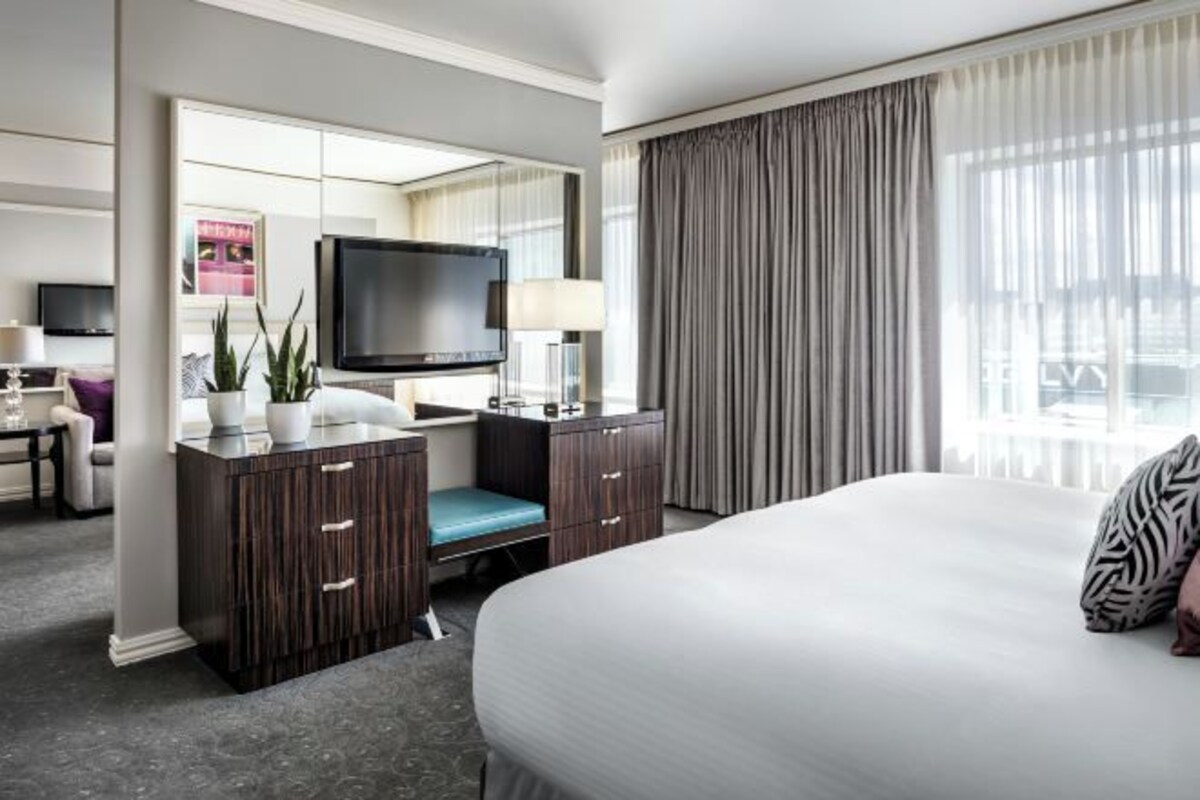 Een hotelkamer met een groot bed, een bureau met stoel, een televisie en een raam met gordijnen.
