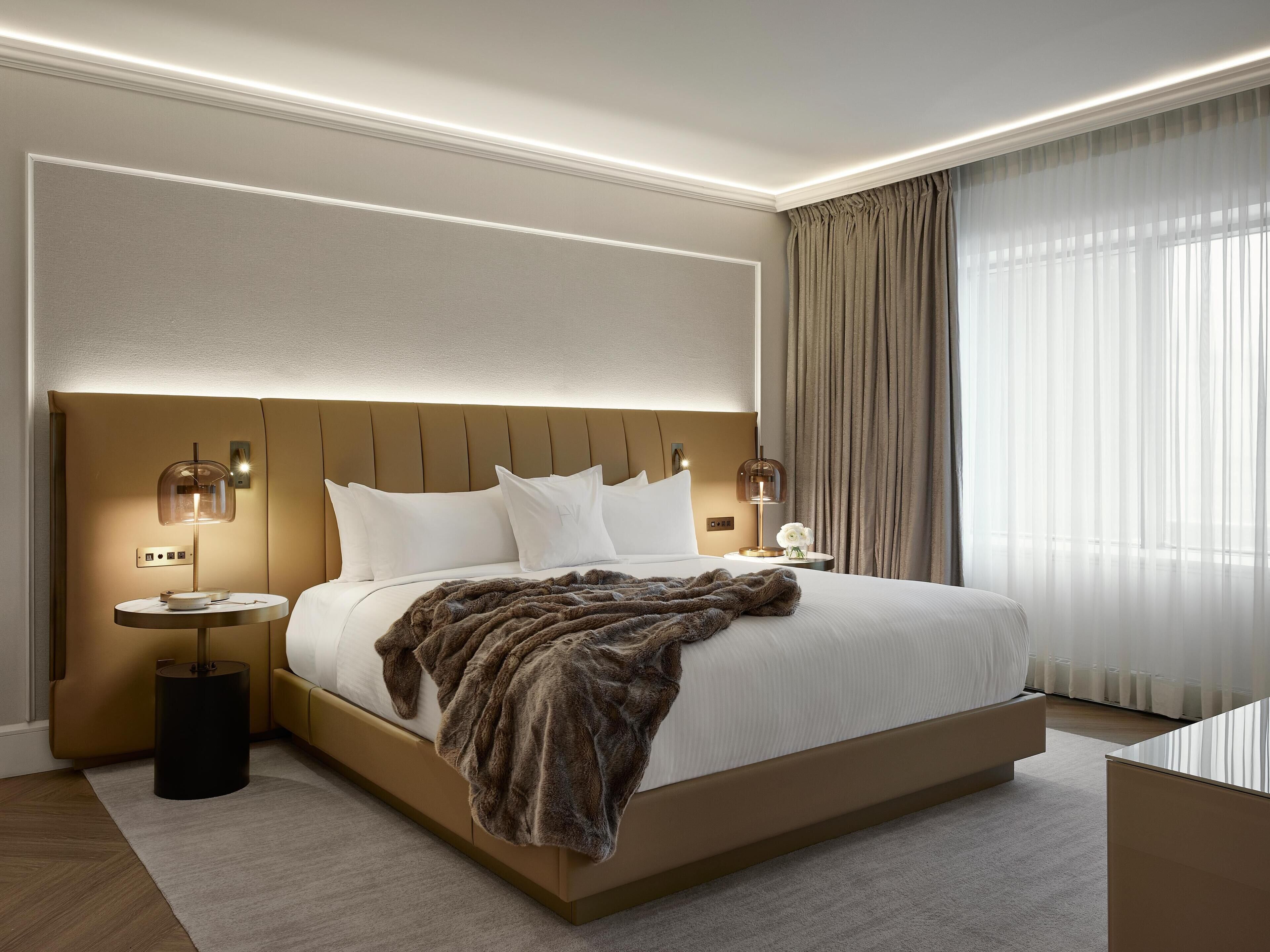 A modern hotel room with a large bed, bedside tables, a nightstand, and a large window with curtains.