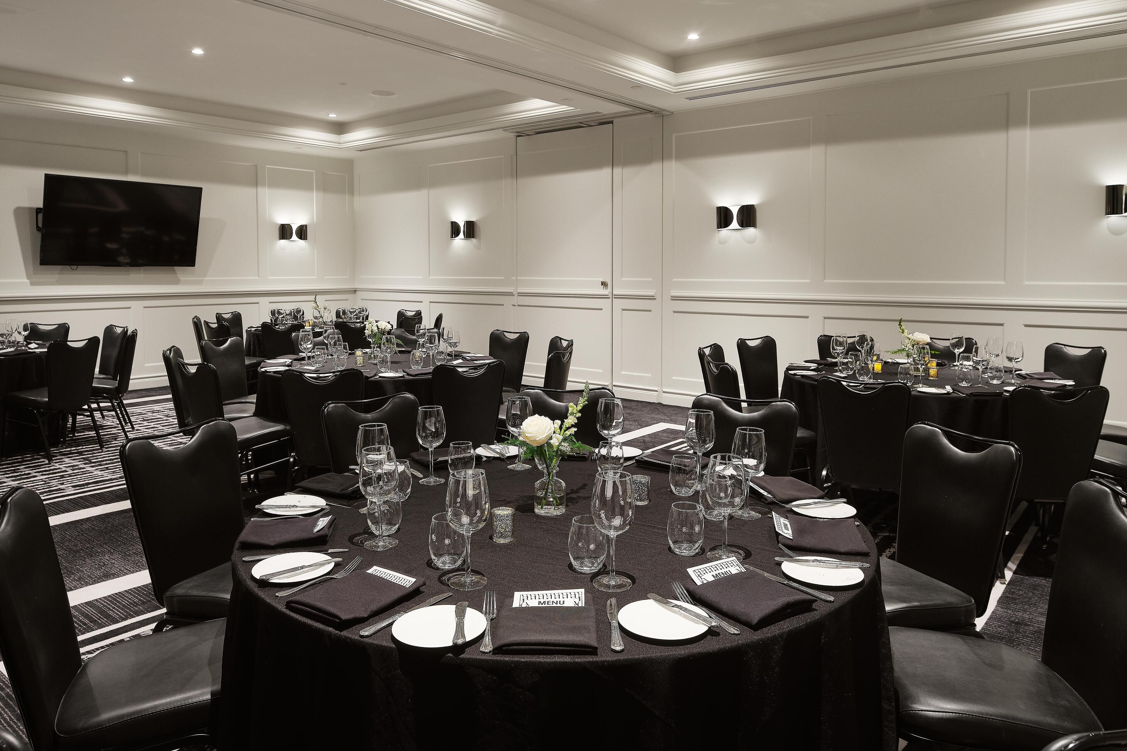A conference room with round tables, black leather chairs, and a large flat-screen TV on the wall.