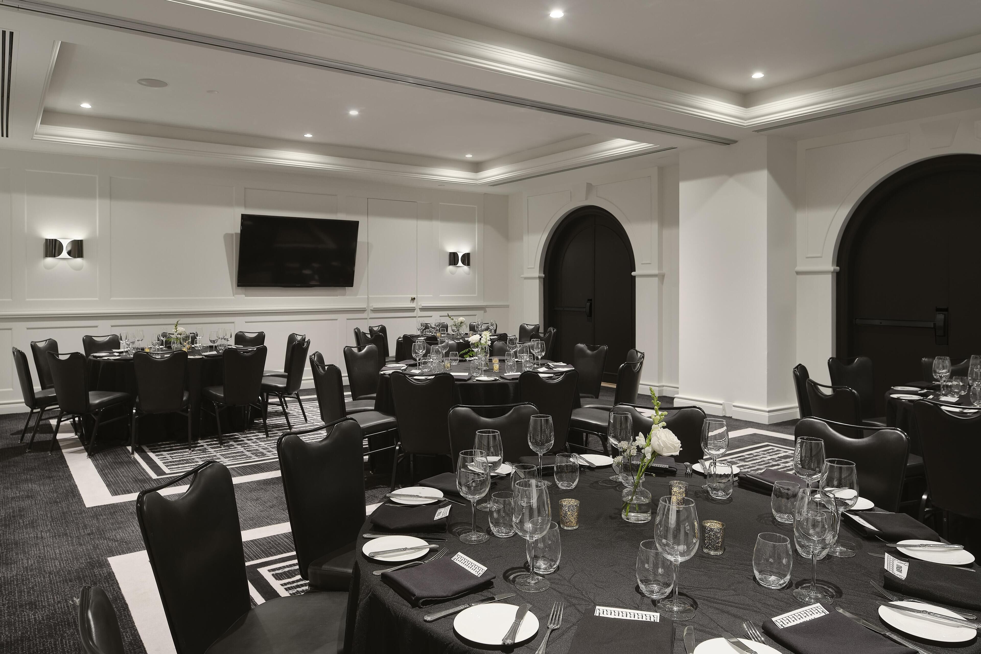Une salle de conférence avec plusieurs tables disposées pour une réunion, équipée de chaises, de tables et d’un téléviseur à écran plat fixé au mur.