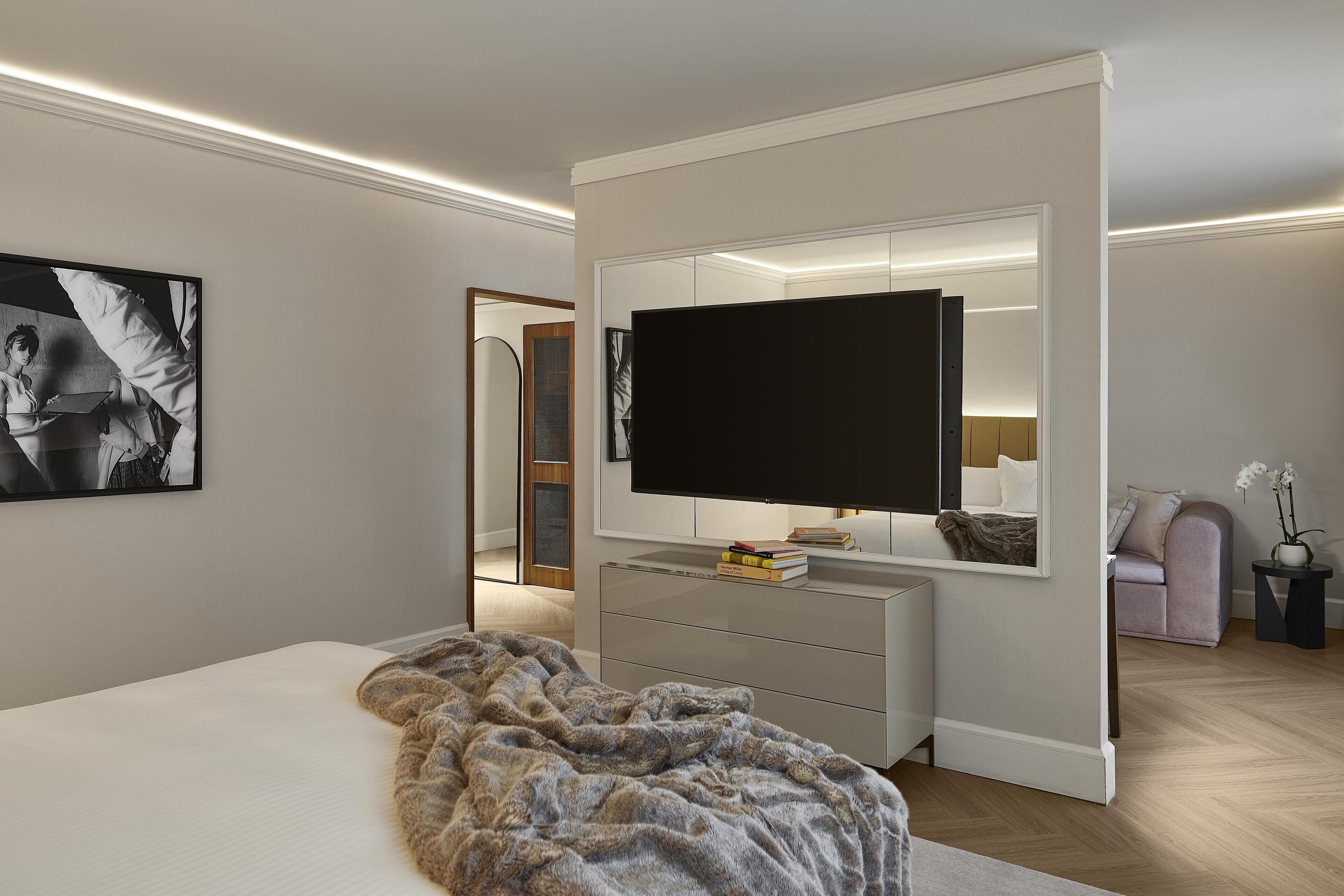 A modern bedroom with a large bed, a TV mounted on a wall, a dresser, and a mirror.