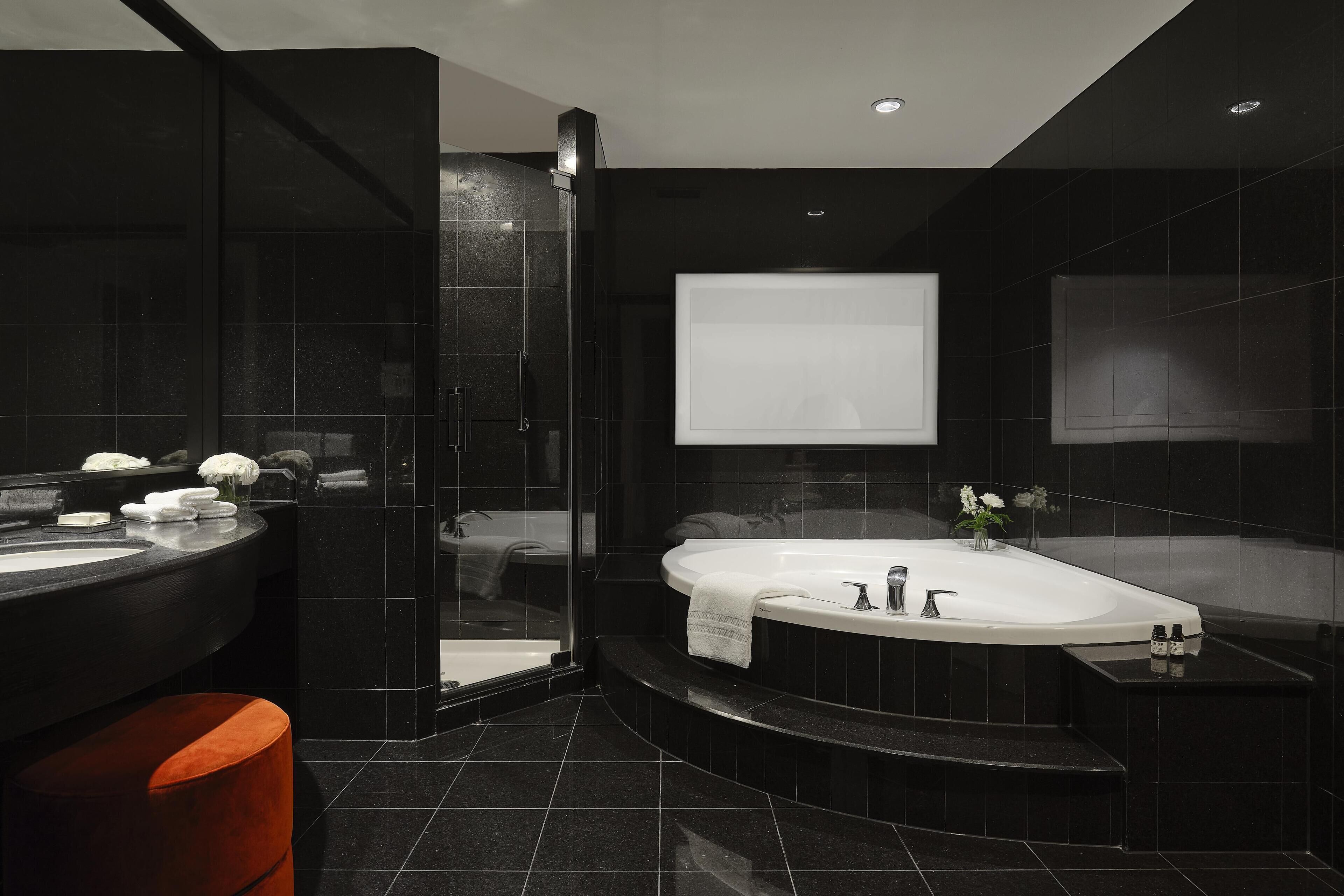 Une salle de bain moderne avec un sol carrelé de couleur noire, une grande baignoire, un espace douche séparé et un meuble-lavabo avec un miroir.
