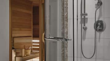 A glass-enclosed shower area with a wooden bench and a sauna visible through the door.