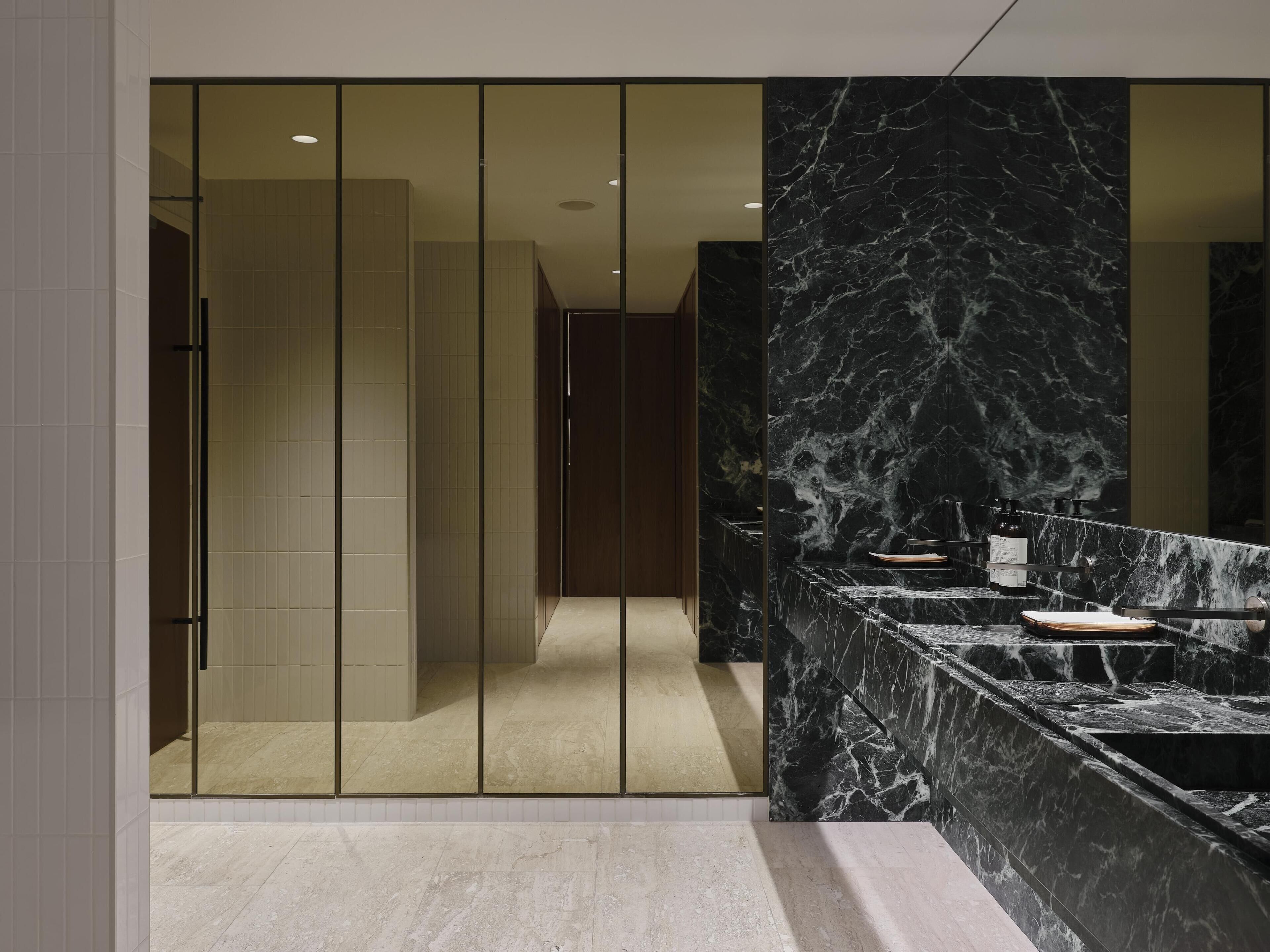 A modern bathroom with a marble countertop, a glass shower enclosure, and a wooden door.