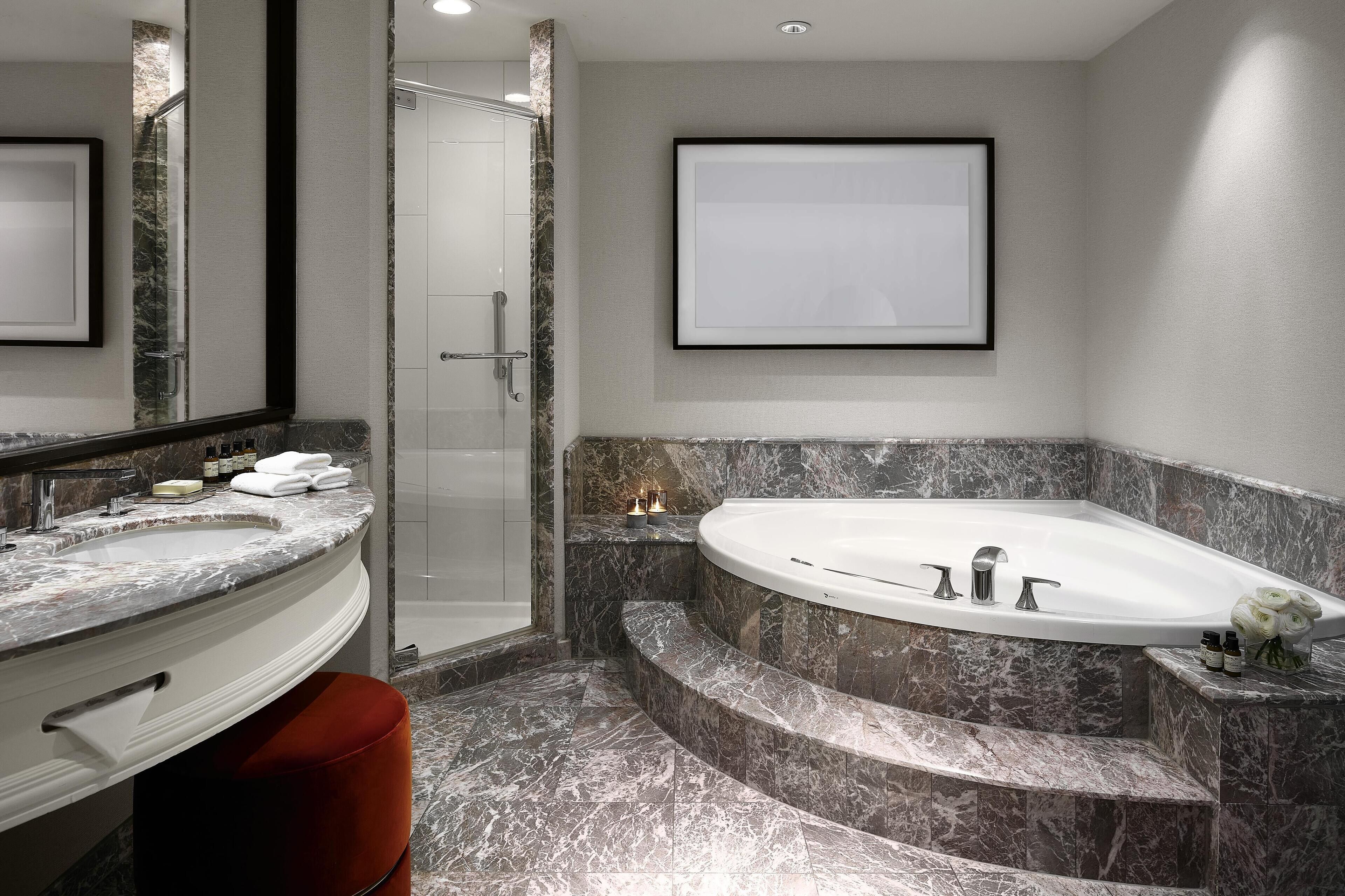 Un baño moderno con un lavamanos grande de mármol, una bañera independiente y una cabina de ducha con paredes de vidrio.