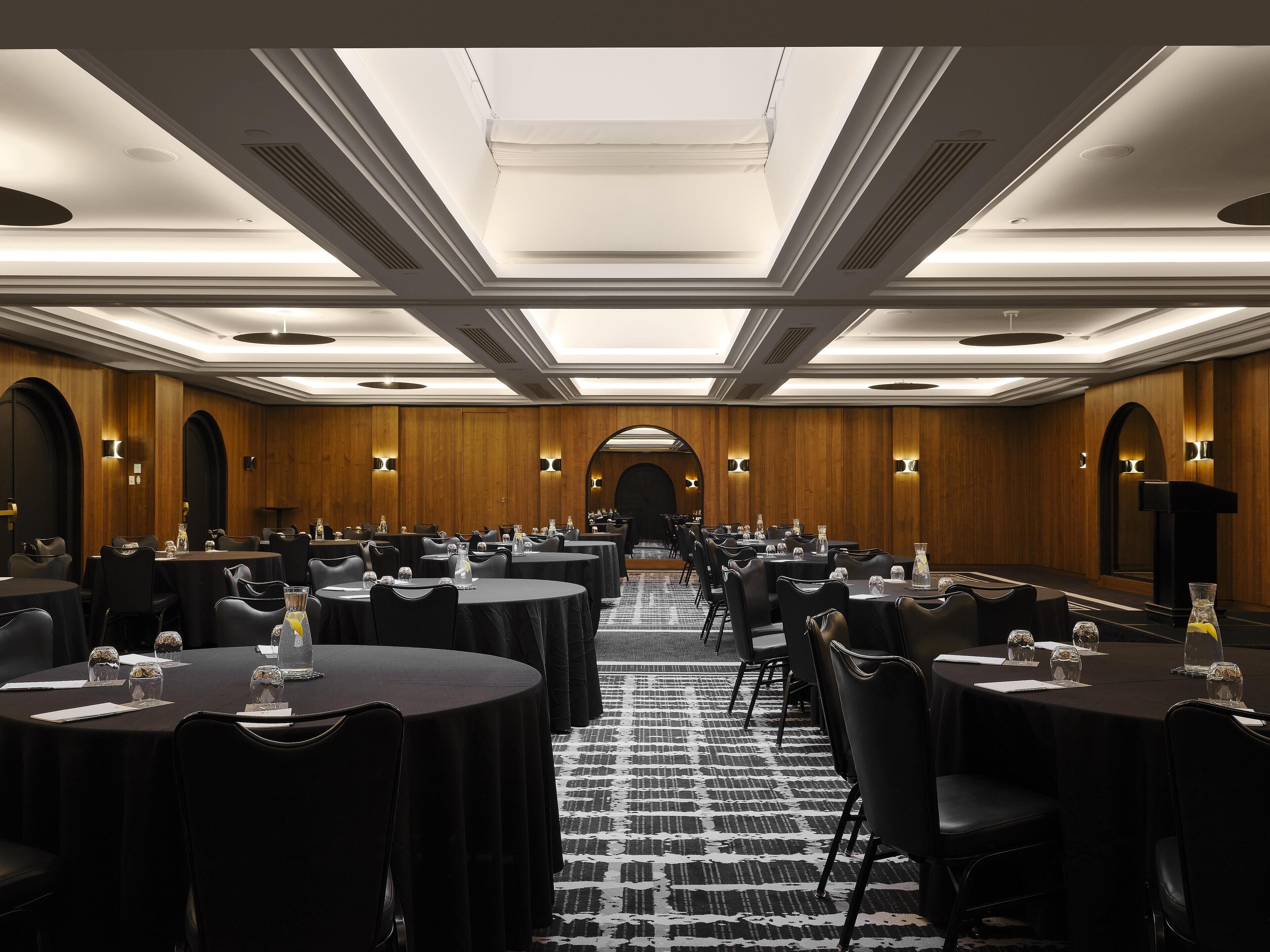 Une salle de conférence avec des tables rondes, des chaises noires et un tapis à motifs.