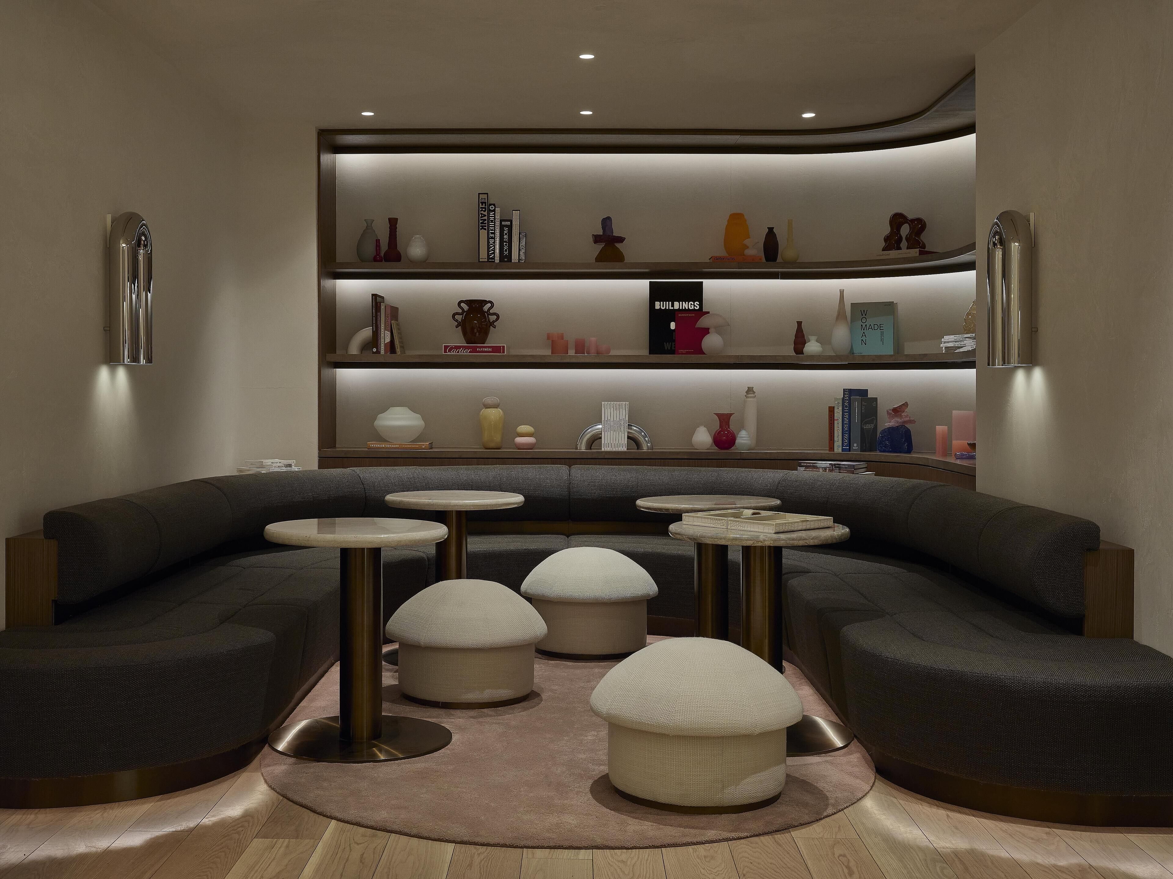 Una sala de estar moderna con un sofá curvo, tres mesas redondas y una estantería con adornos.