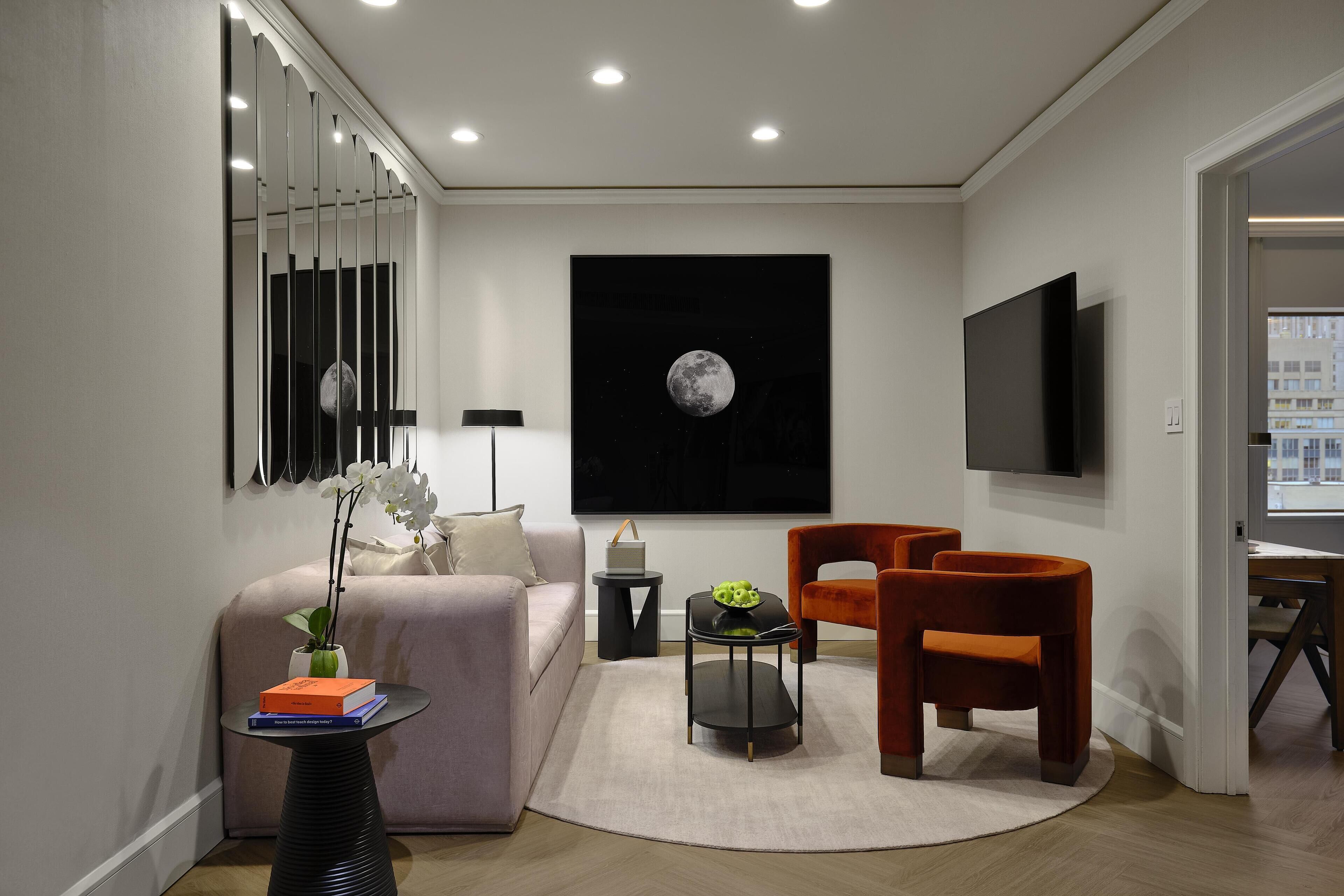 A modern living room with a sofa, two armchairs, a coffee table, a side table, a floor lamp, a television, and a wall-mounted artwork of the moon.