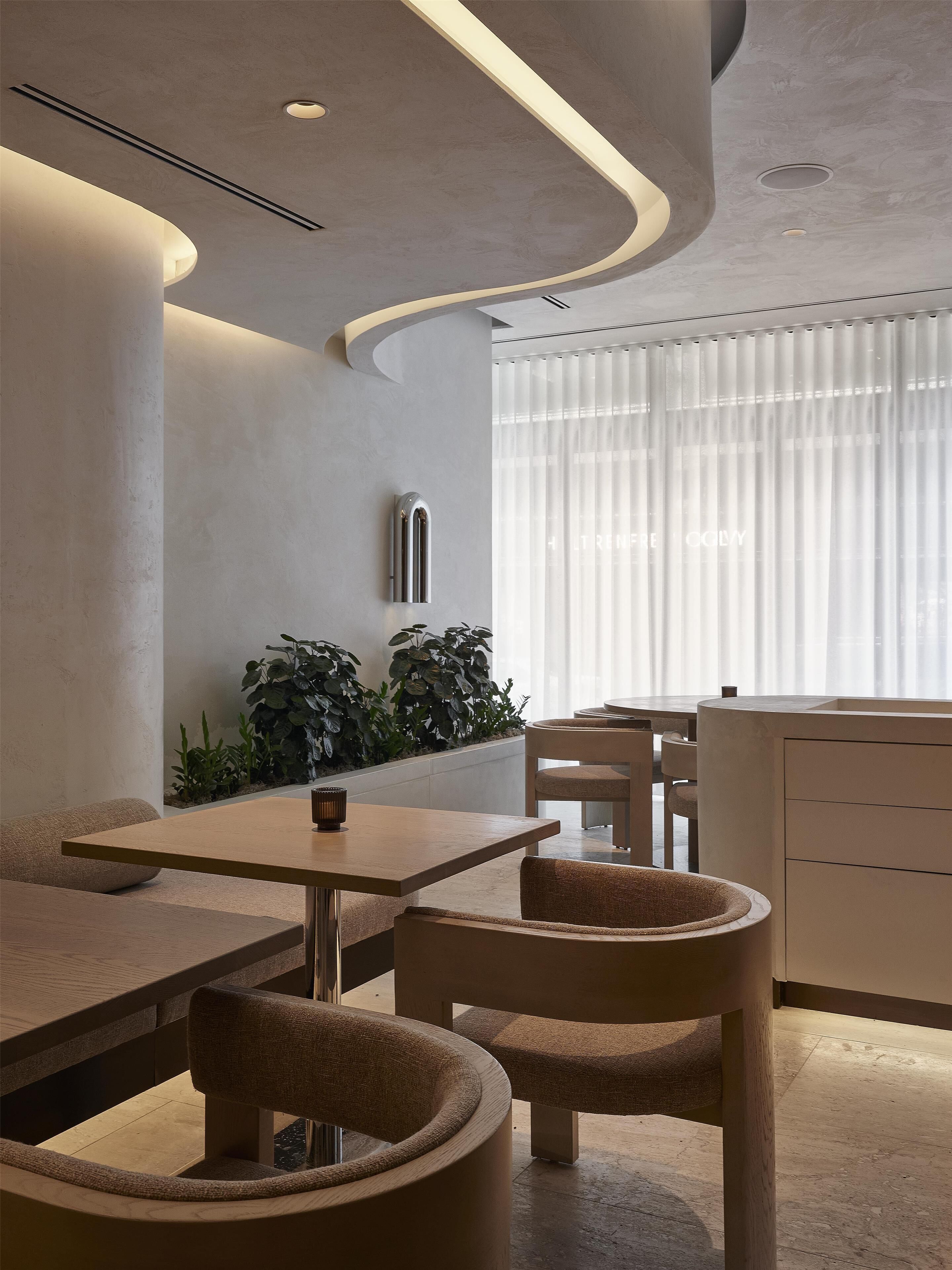 A modern interior with a curved ceiling, recessed lighting, a dining area with a table and chairs, and a plant wall.