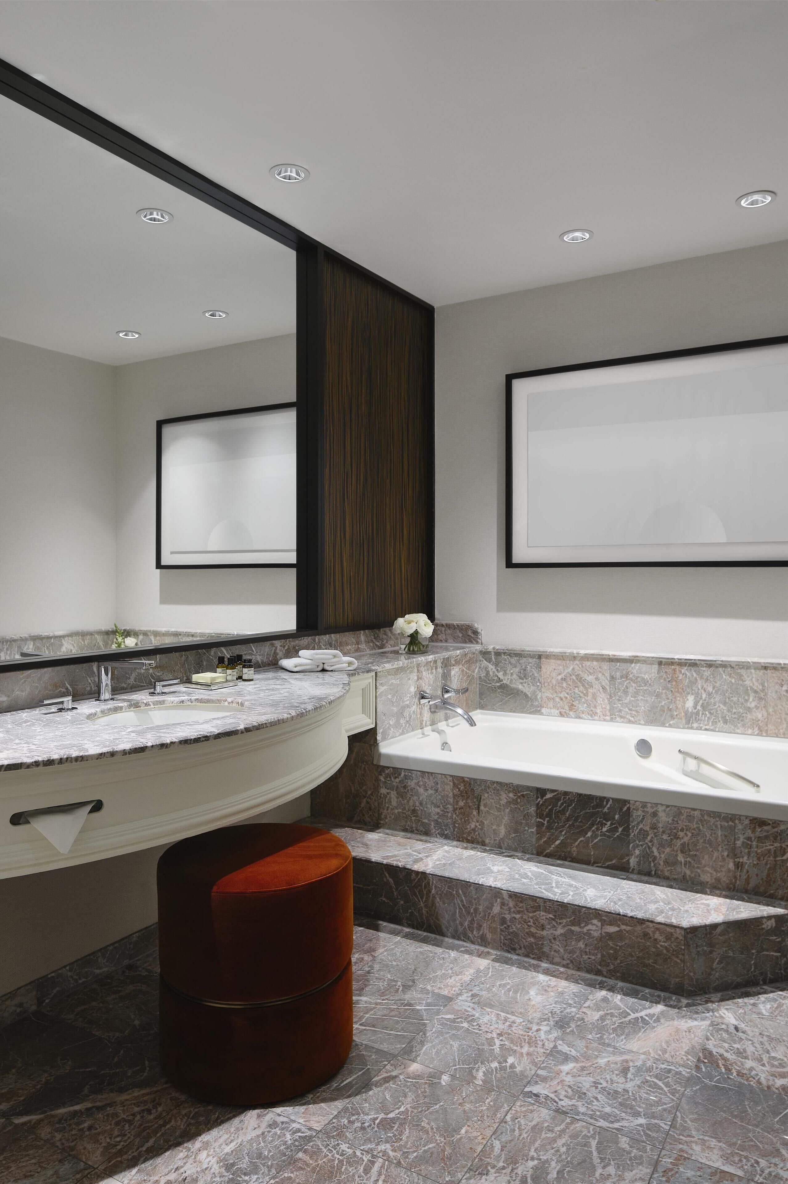A modern bathroom with a large mirror, two sinks, a bathtub, and a red stool.