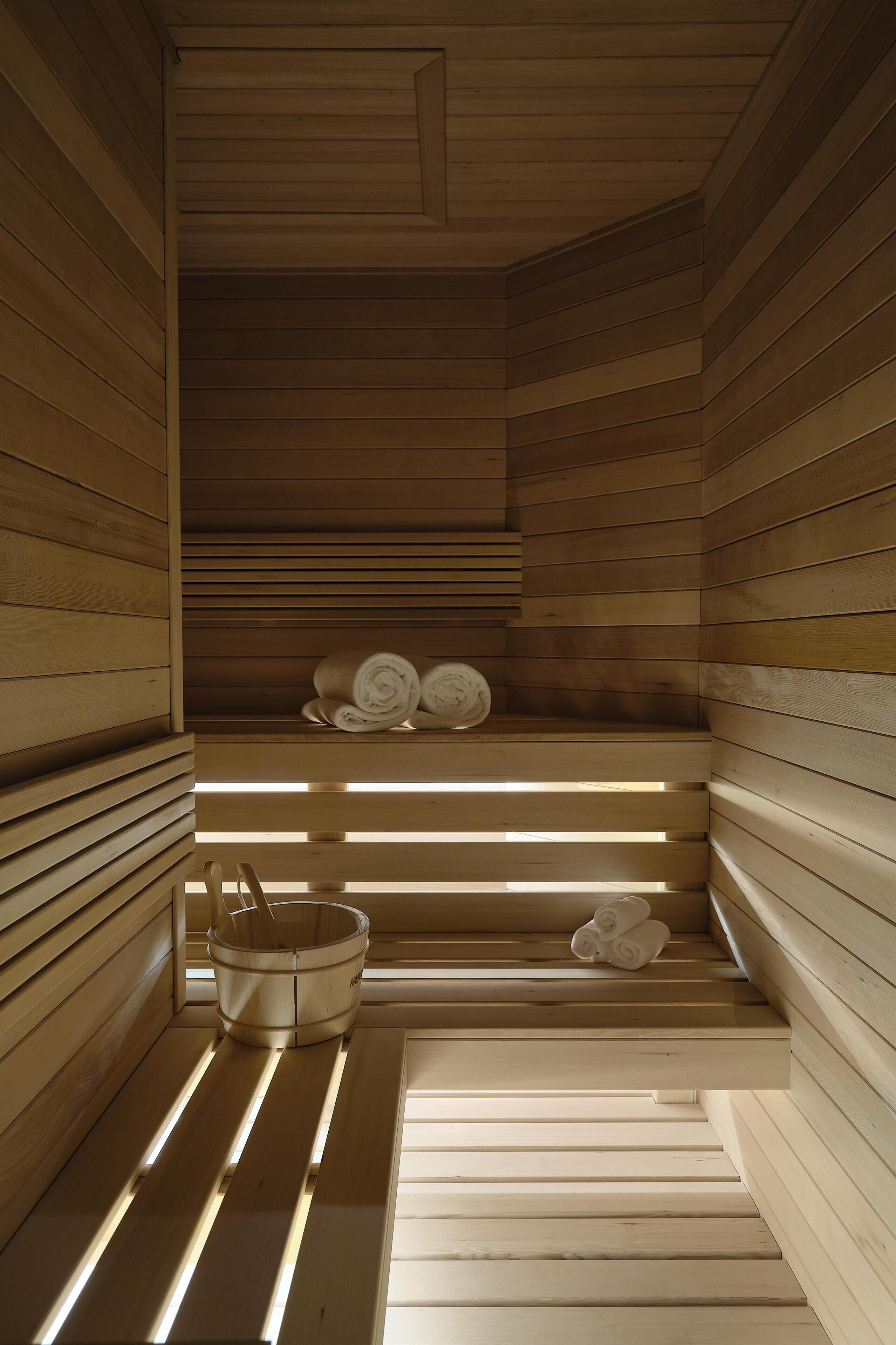 A sauna with wooden slats, a wooden bench, and a bucket with towels.